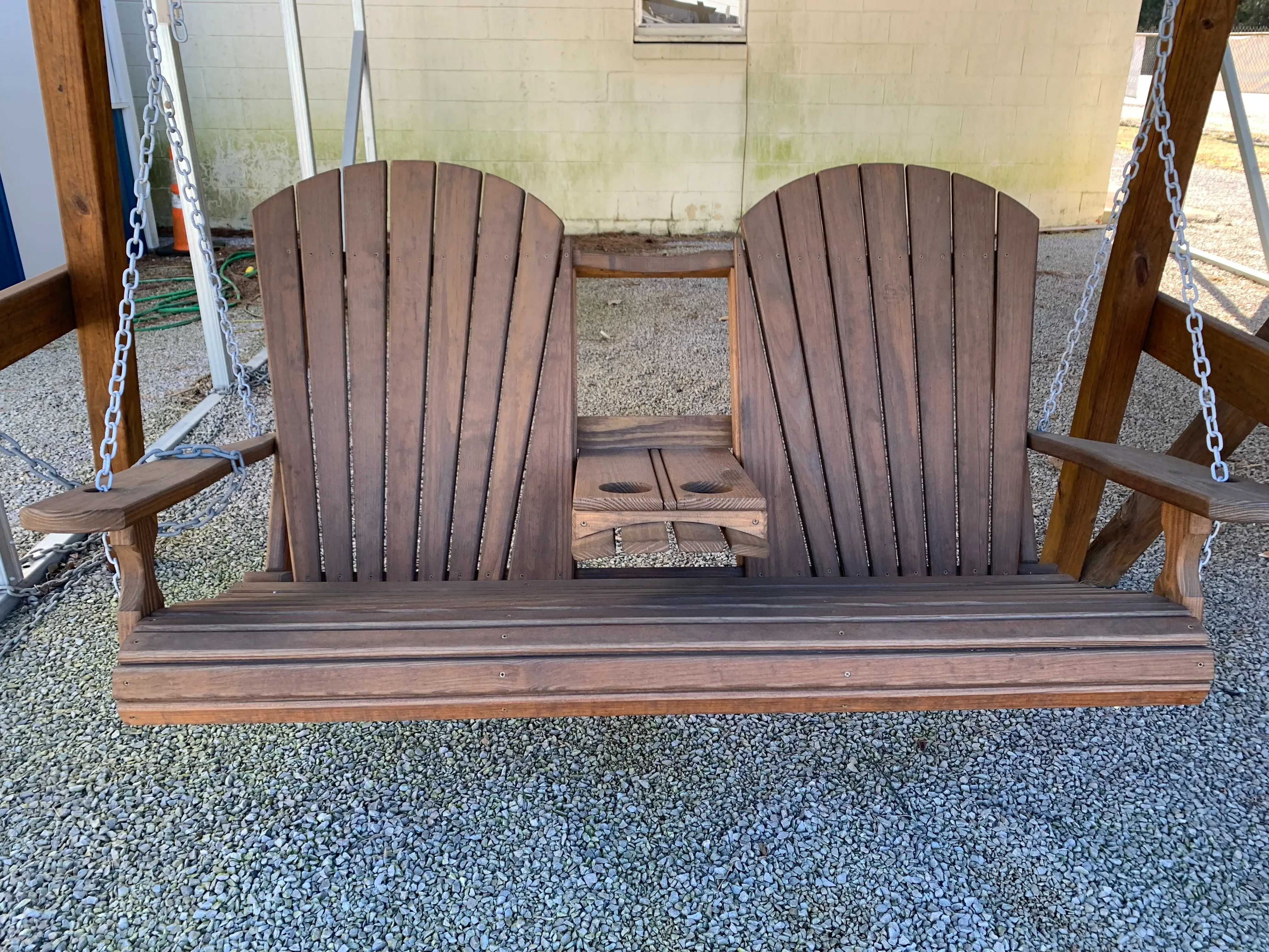 a wood bench swing hovering over gravel. It is stained and sealed. It is attached to a wooden a-frame structure by chains