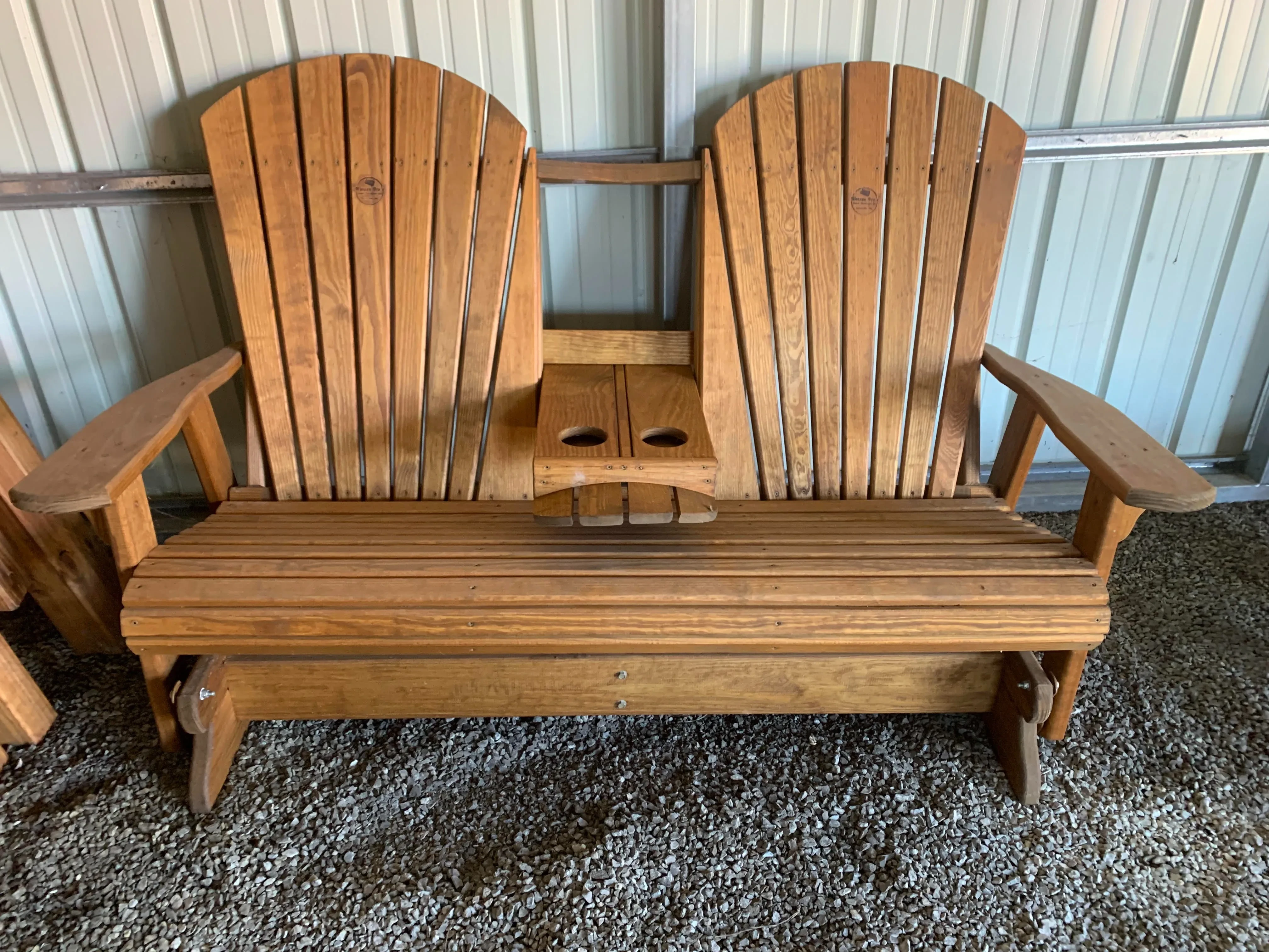 a wood stained and sealed bench sitting in gravel. It has a center console that flips up and down, with two cupholders.
