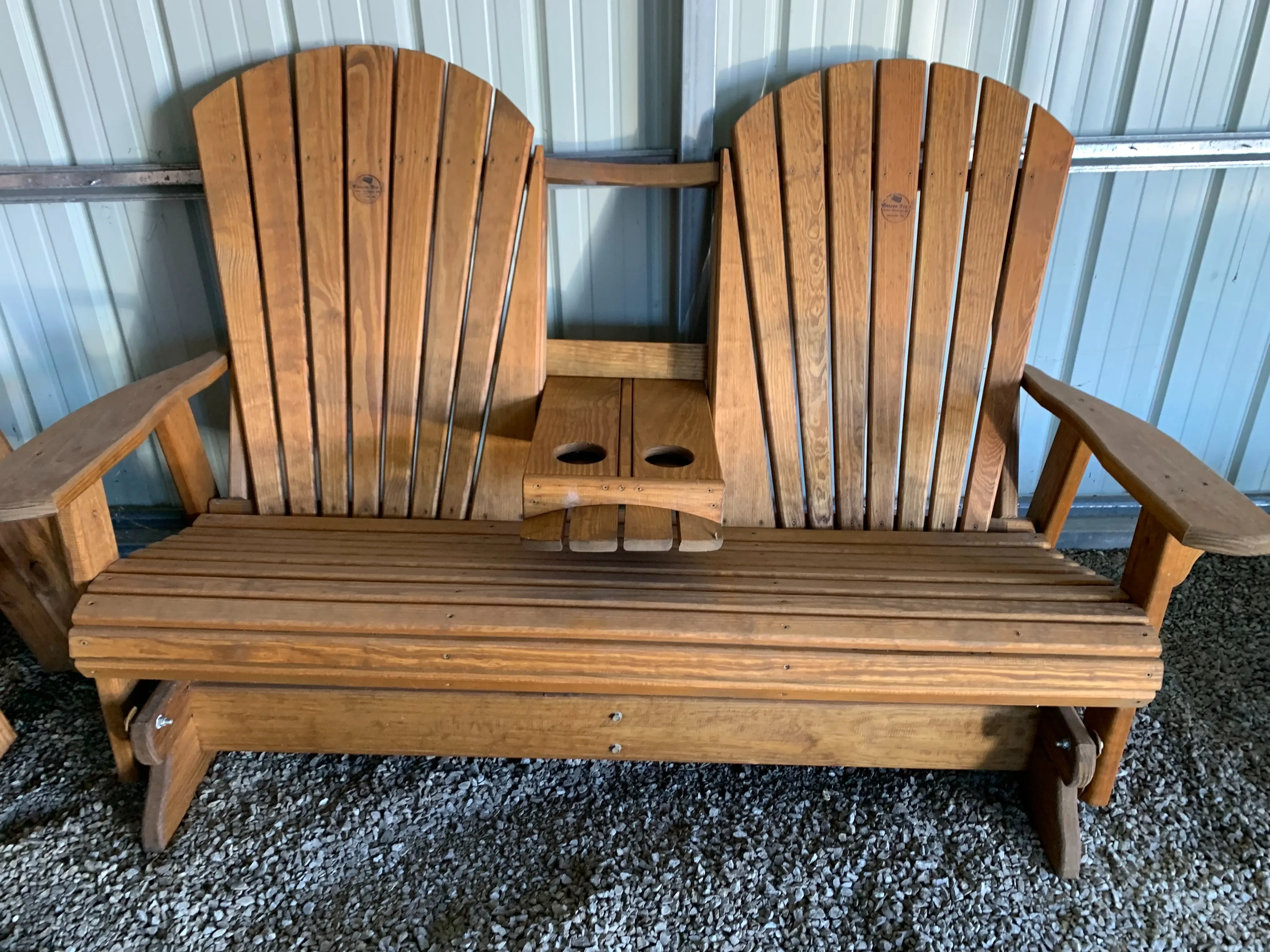 a wood bench that glides back and forth sitting in the gravel. It is stained and sealed. It has a center console