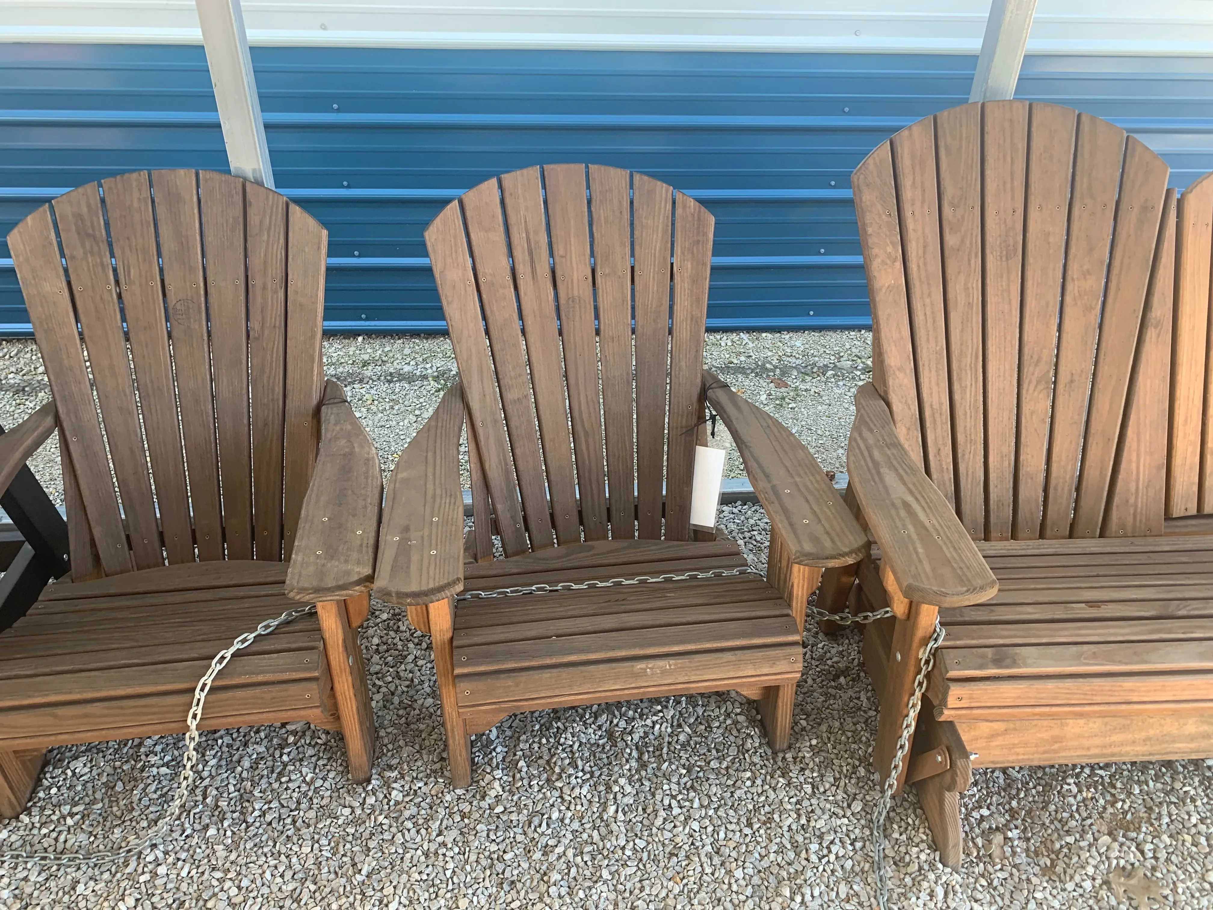 a chair sitting in the gravel. It is stained and sealed. It has armrests. It has a white price tag on the arm rest