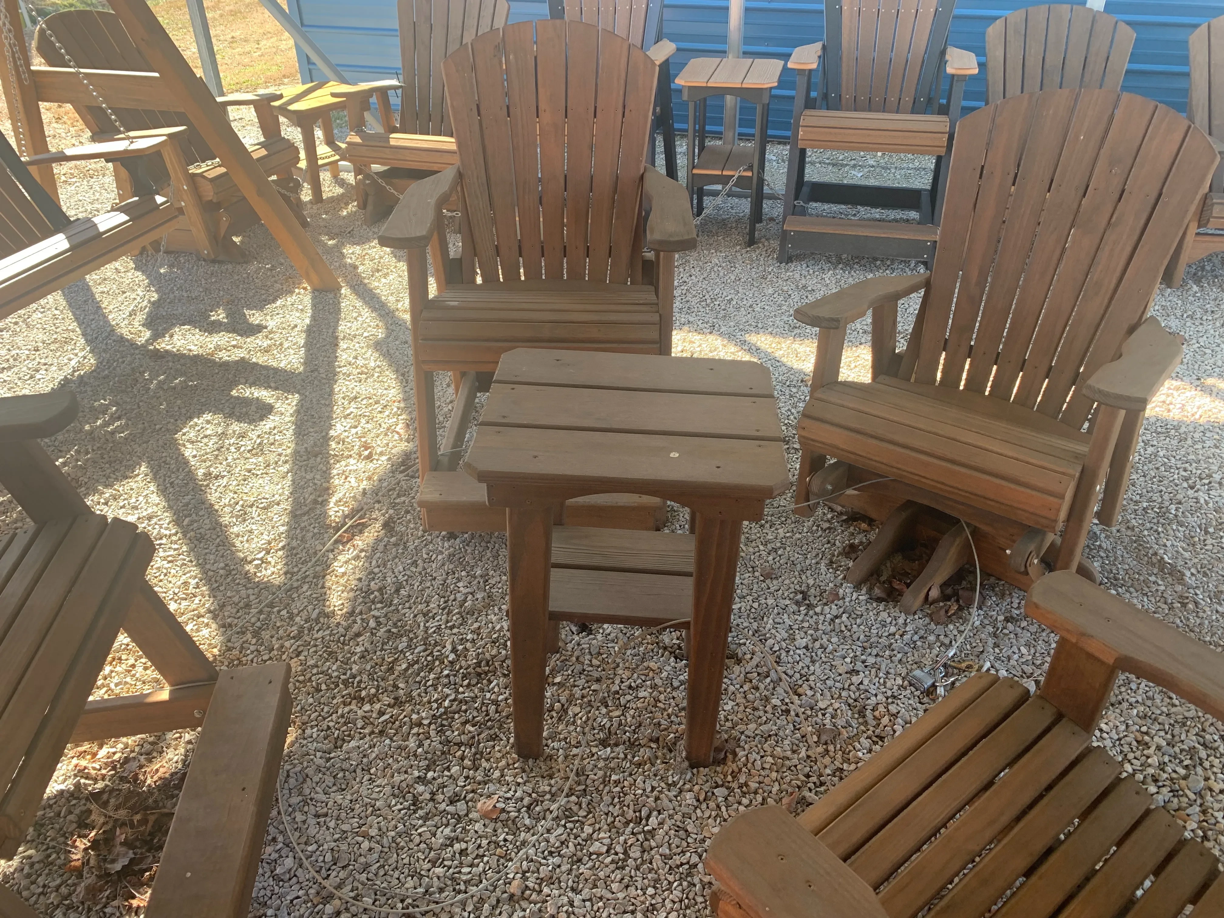 a wood stained and sealed table sitting in the gravel. It is surrounded by chairs.