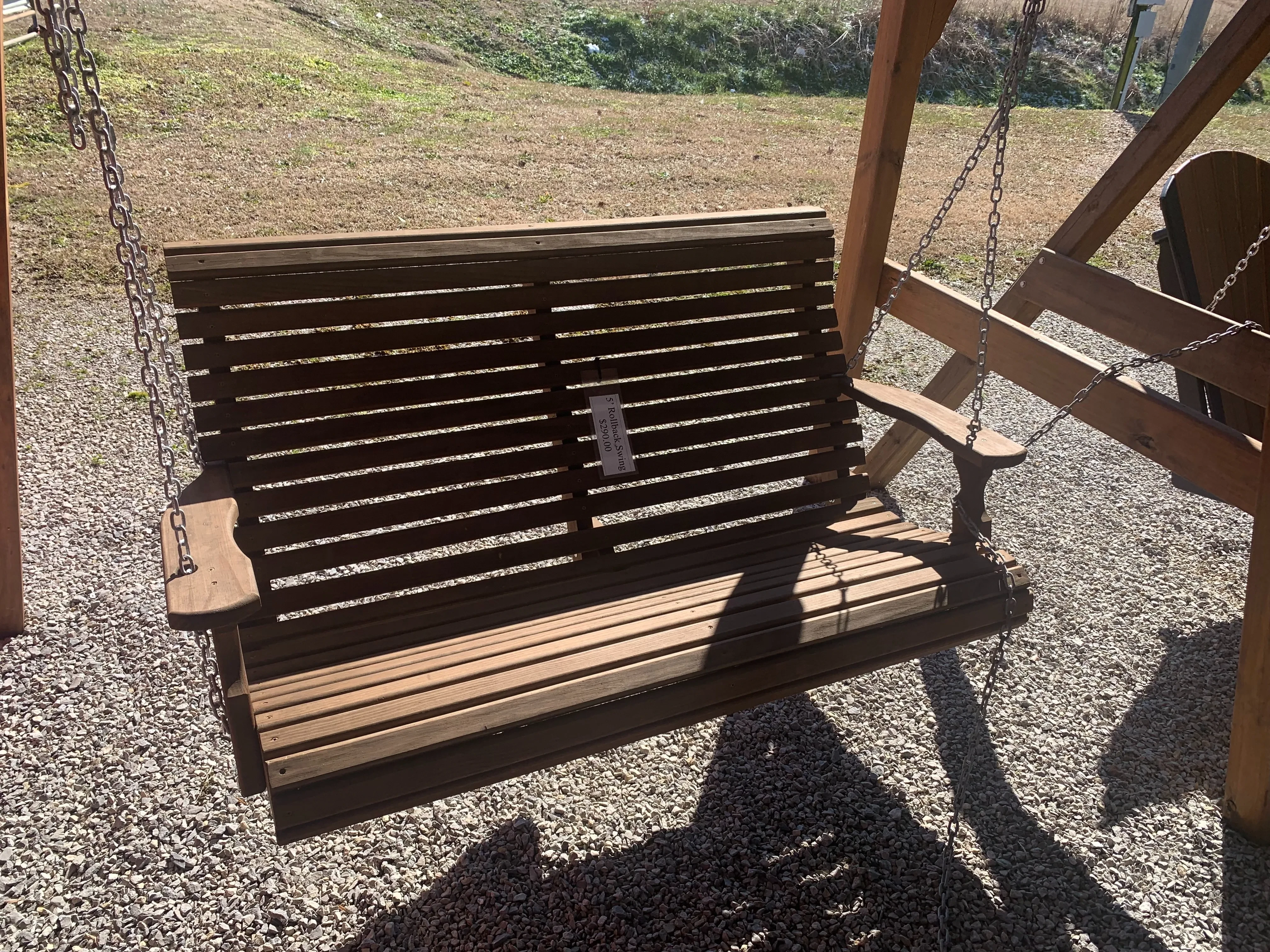 a bench swing hovering over gravel. It is stained and sealed professionally. It has a white price tag on the front of it