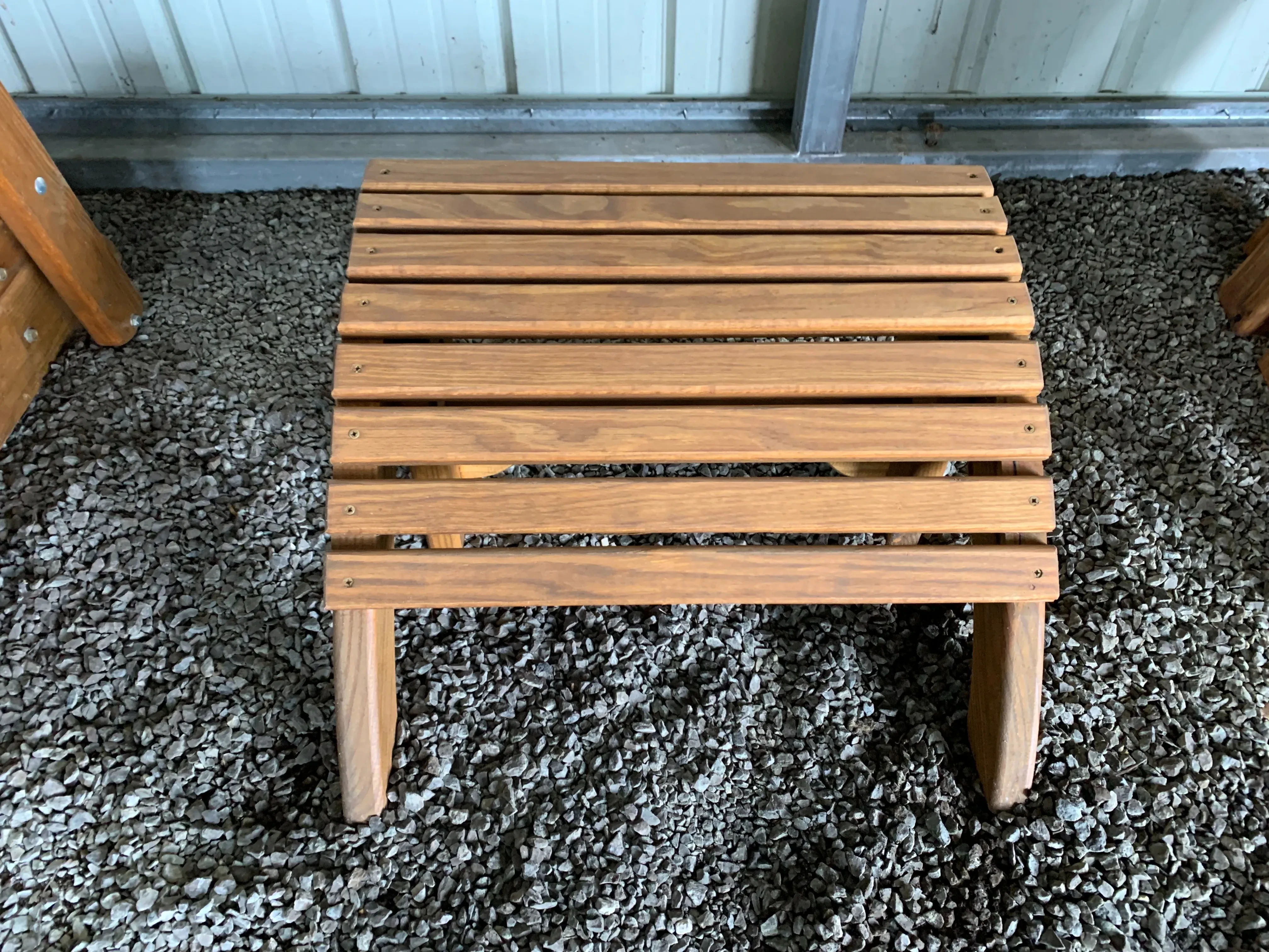 a footstool sitting in the gravel. It is stained and sealed. It has eight slats running horizontally