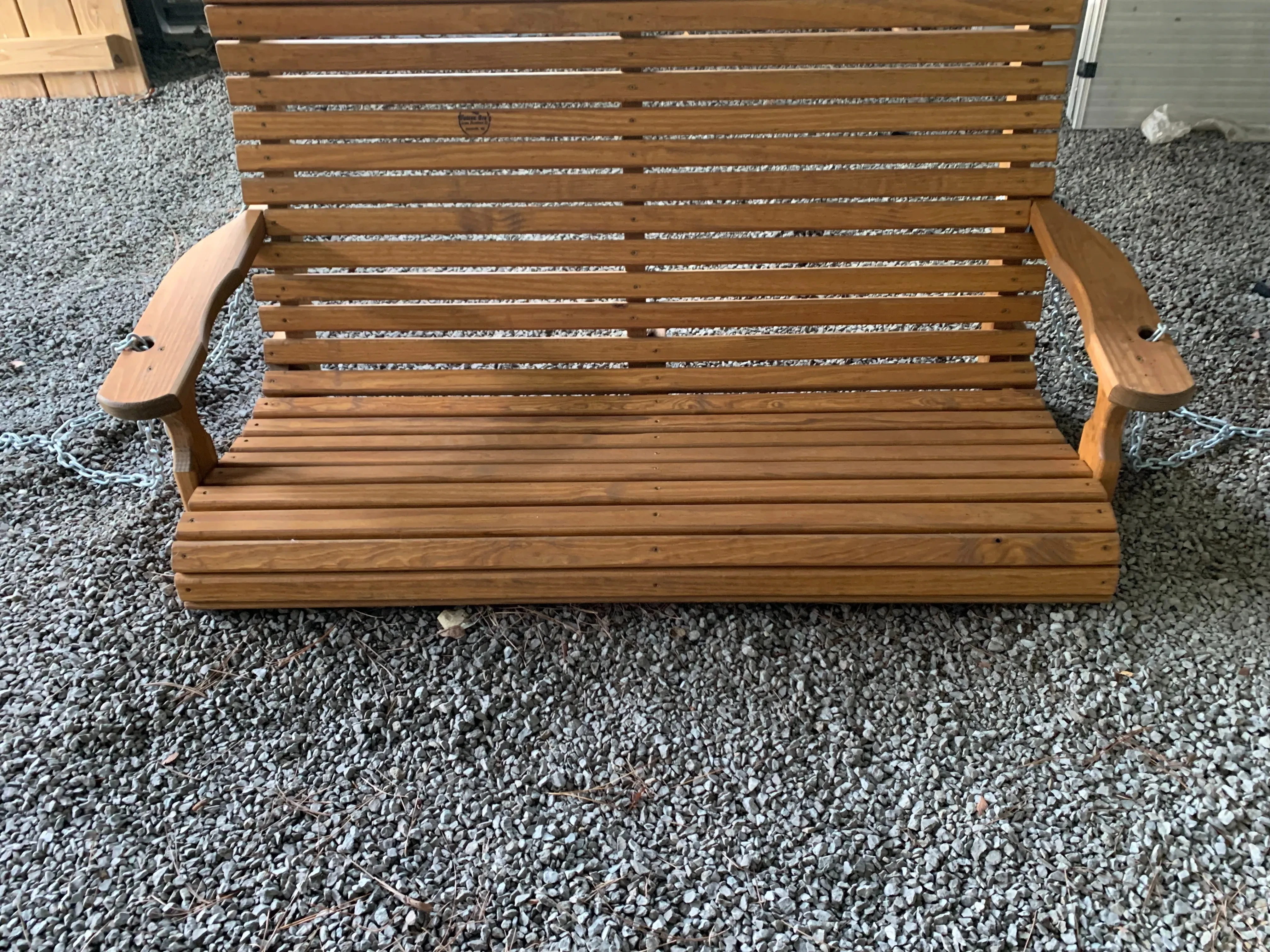 a wood stained and sealed bench sitting on the gravel. It has slats running horizontally.