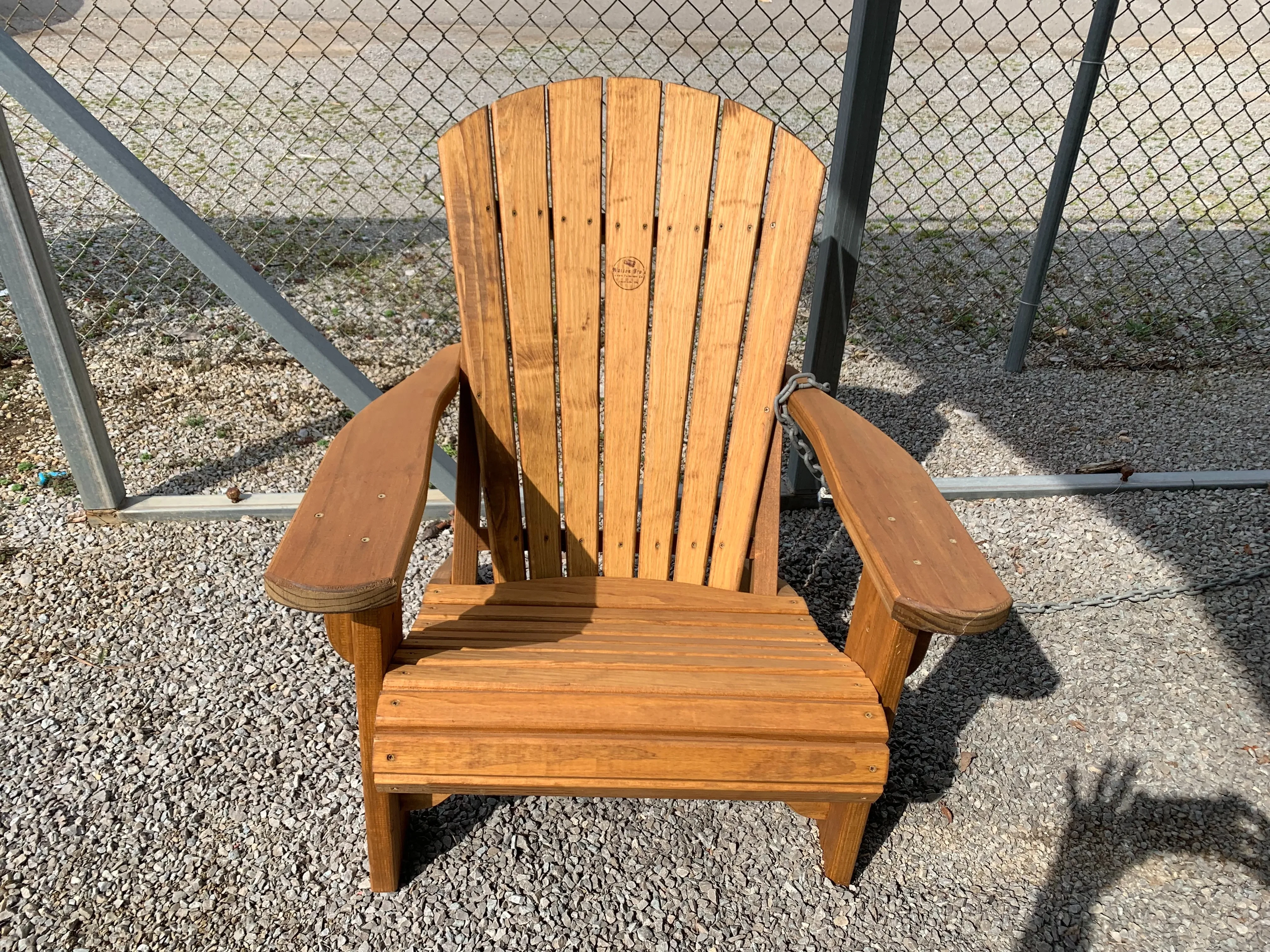 a wood stained and sealed chair sitting in the gravel. It has a chain hooked up to it.