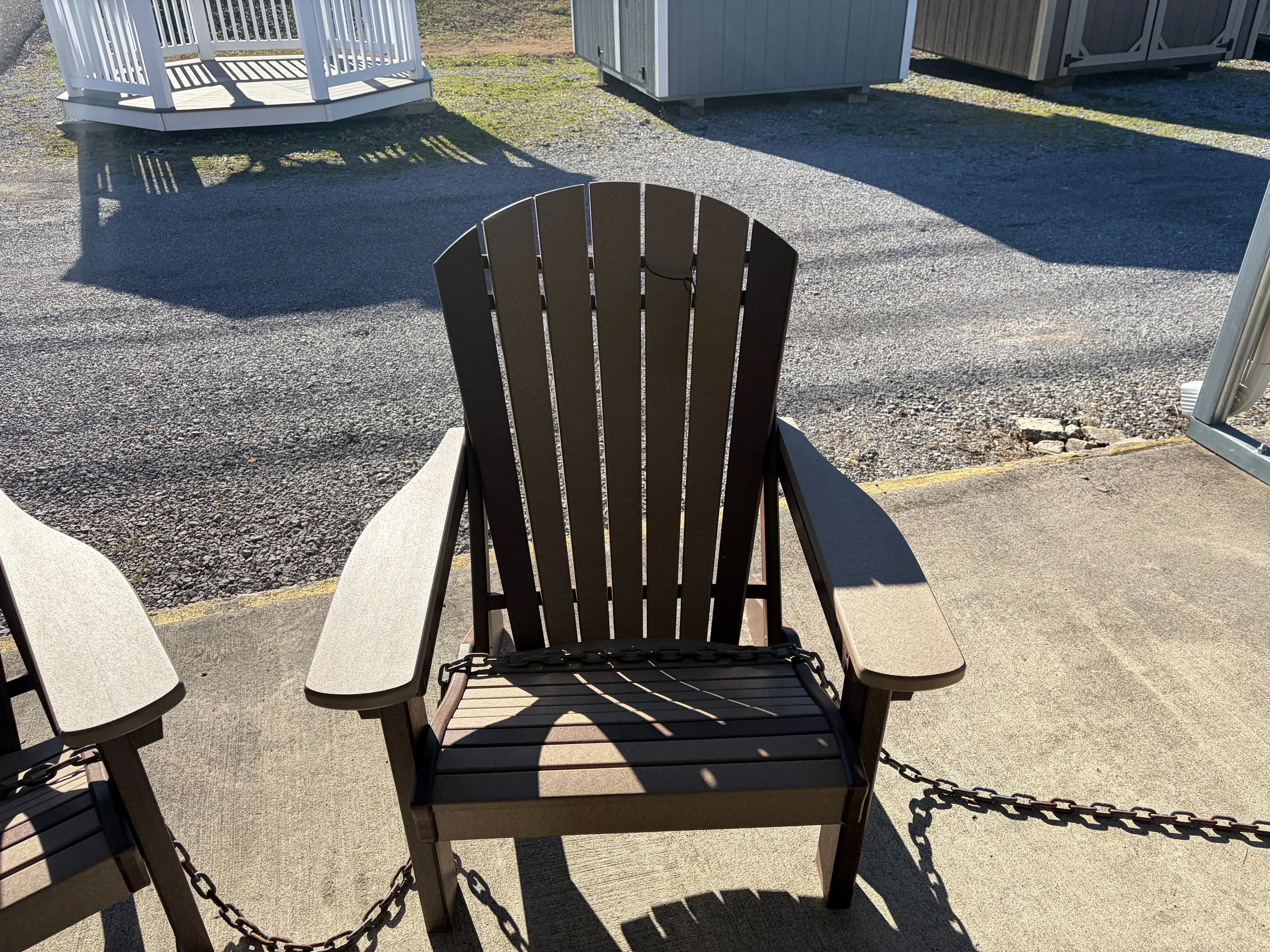 a chair sitting on concrete. It is made out of a polywood material. It is light brown with dark brown accents.