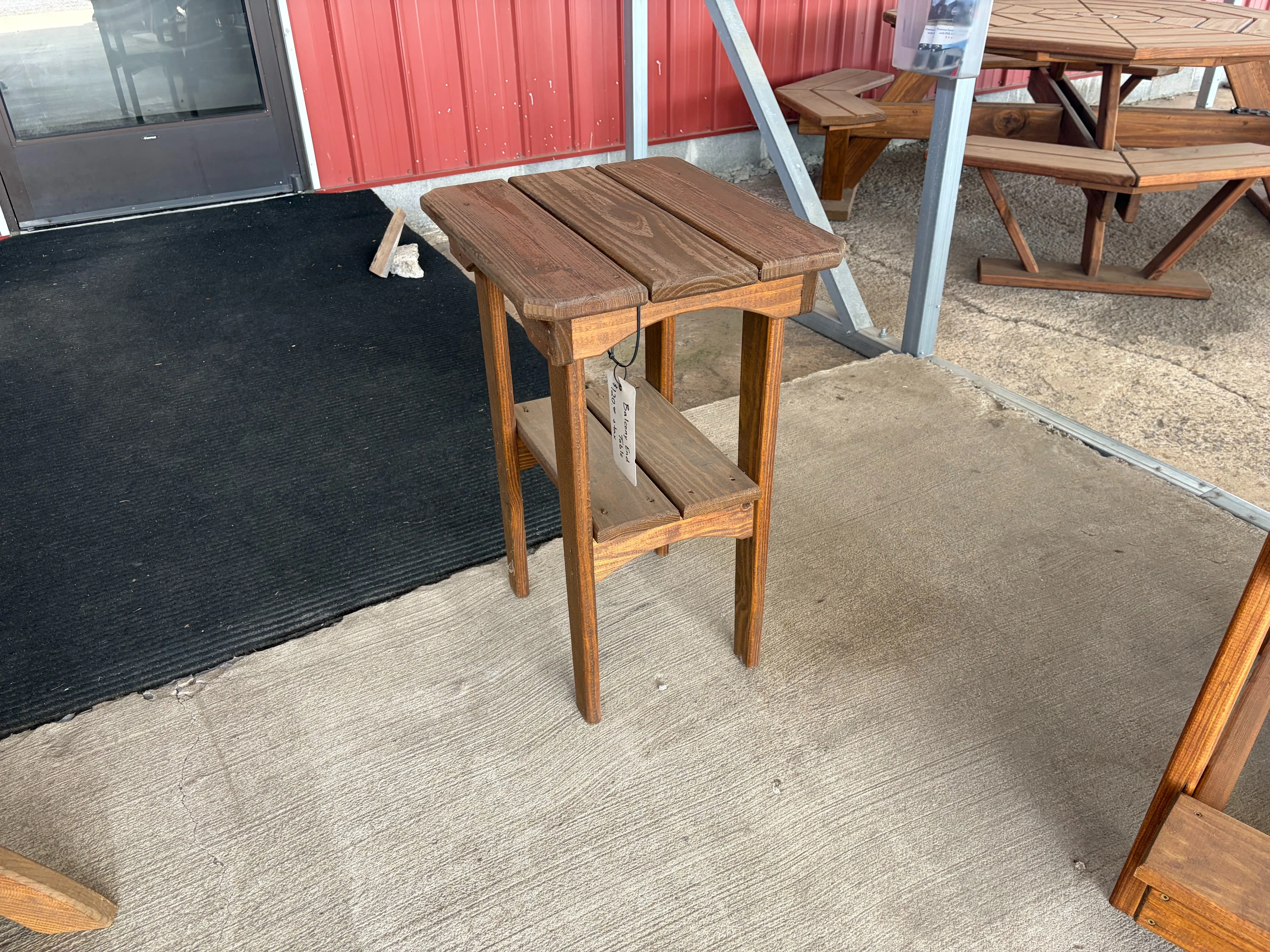 a table sitting on concrete. It is stained and sealed. There is a carpet next to it. There is a white price tag on it