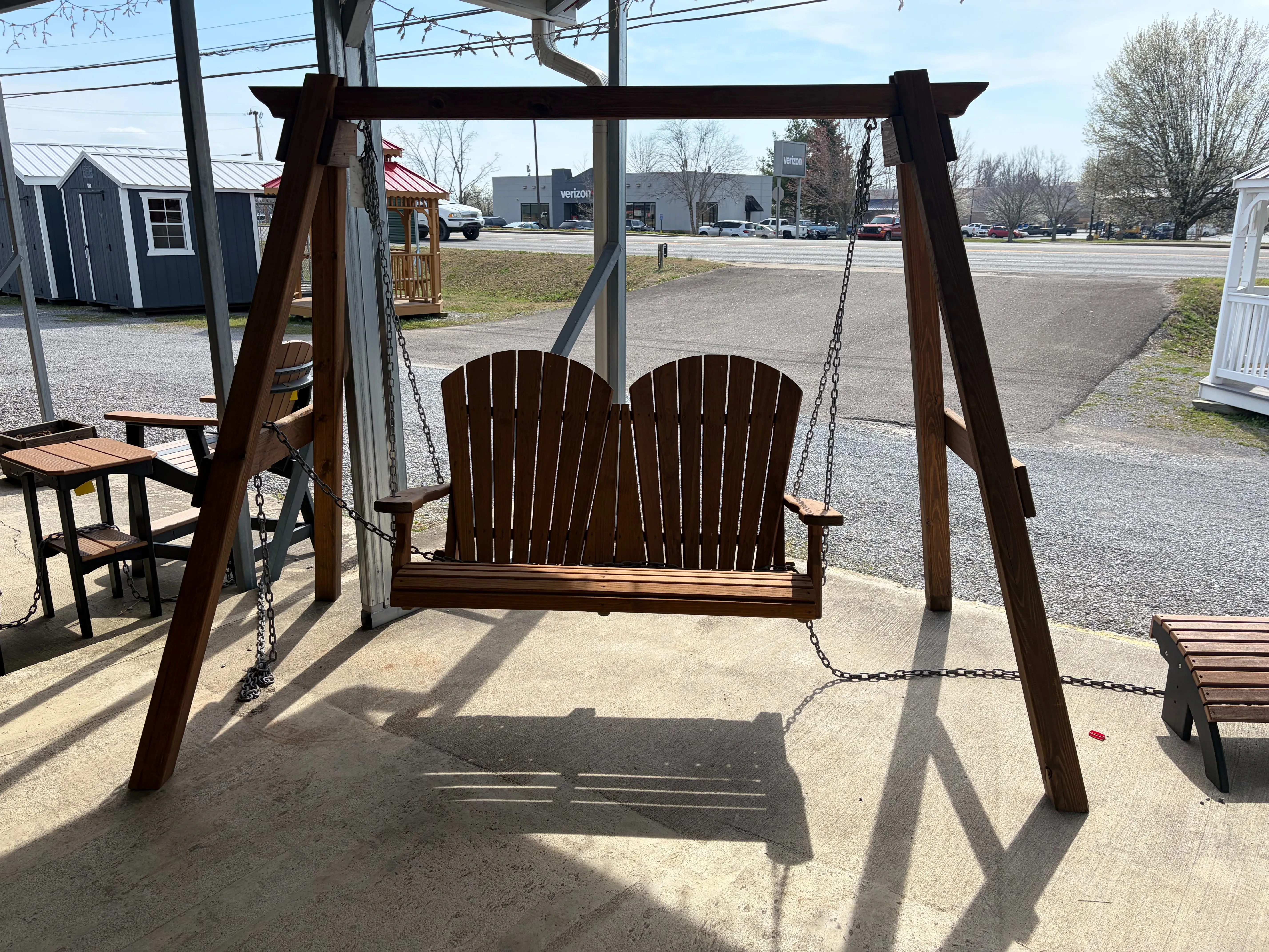 a bench swing attached to a wooden a-frame structure standing on concrete. There are sheds behind it.