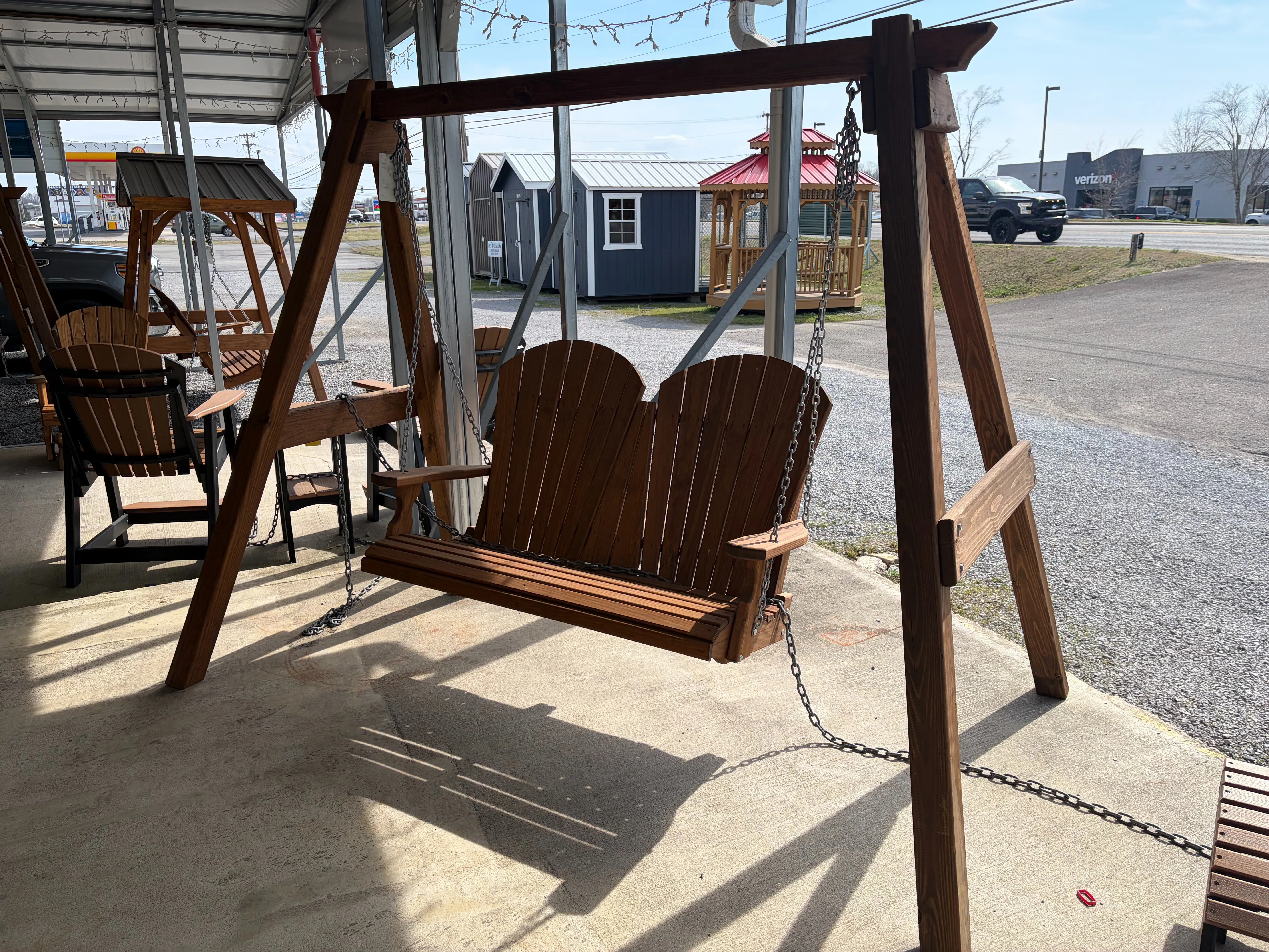 a wooden a-frame structure holding up a wood stained and sealed bench swing. It is chained up to other furniture nearby