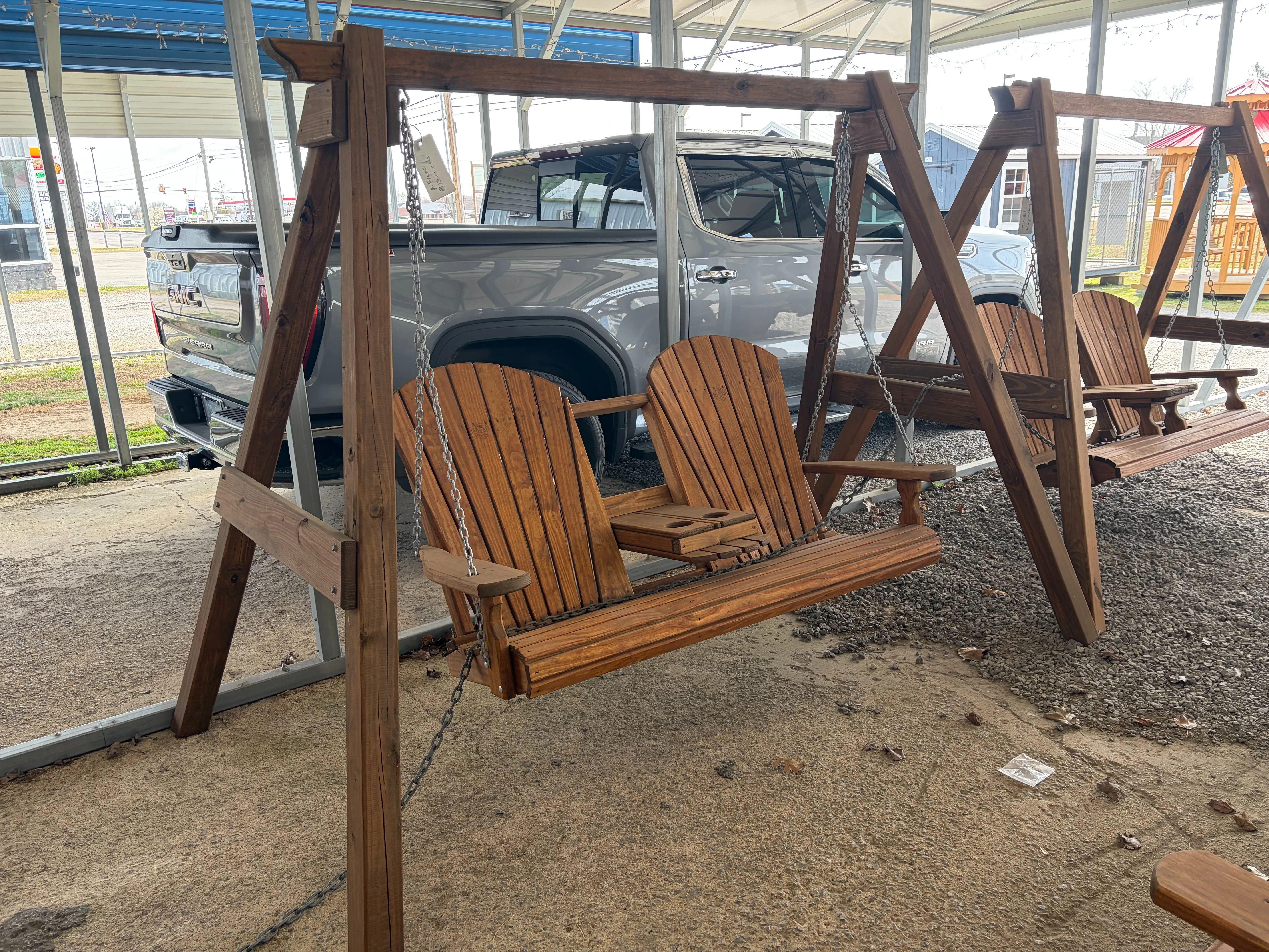 a stained and sealed bench swing attached to a wood a-frame structure. There is a gray truck directly behind it.