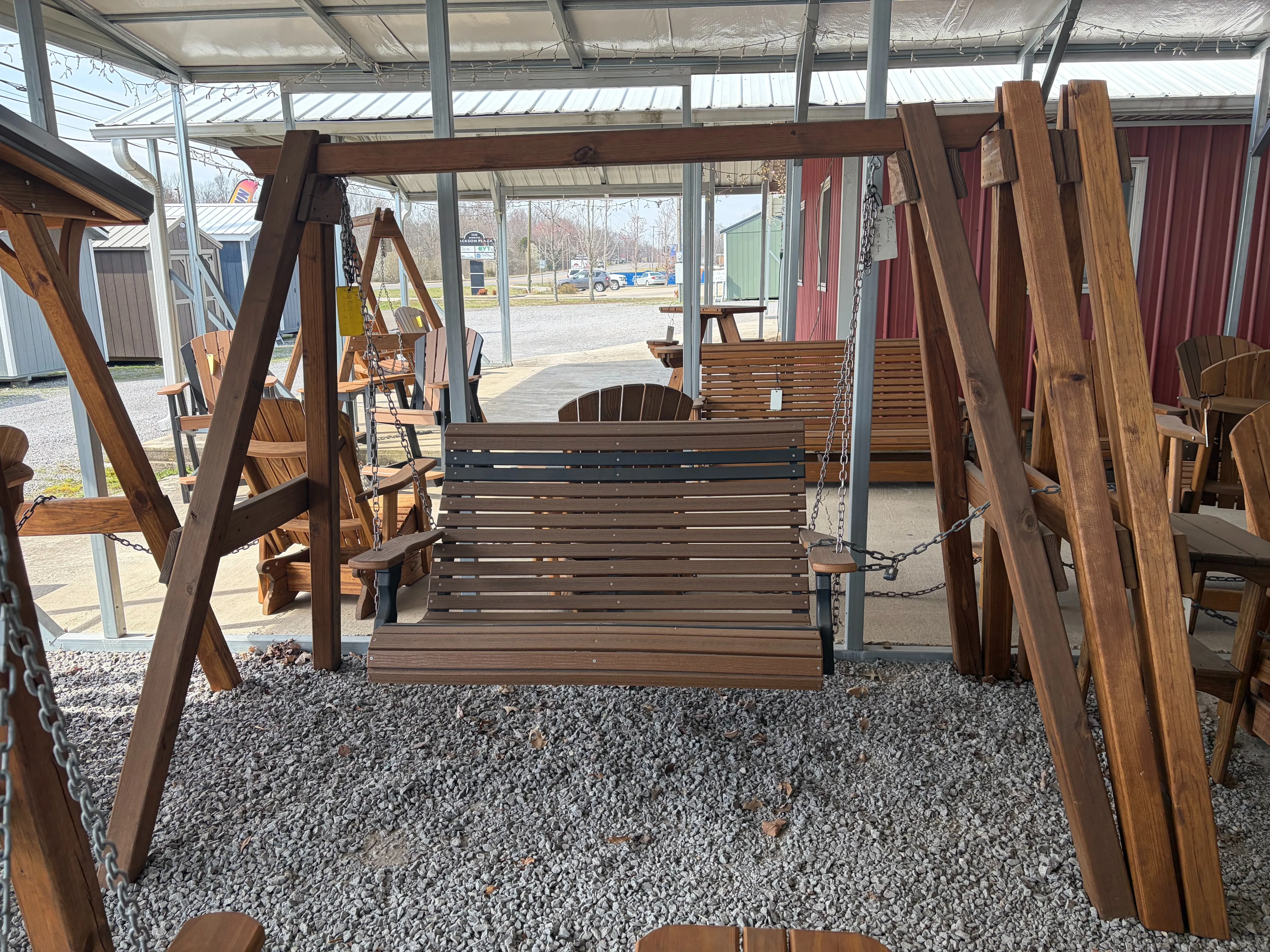 a polywood bench that is brown with black accents attached to a wooden a-frame structure with chains. It is on gravel.