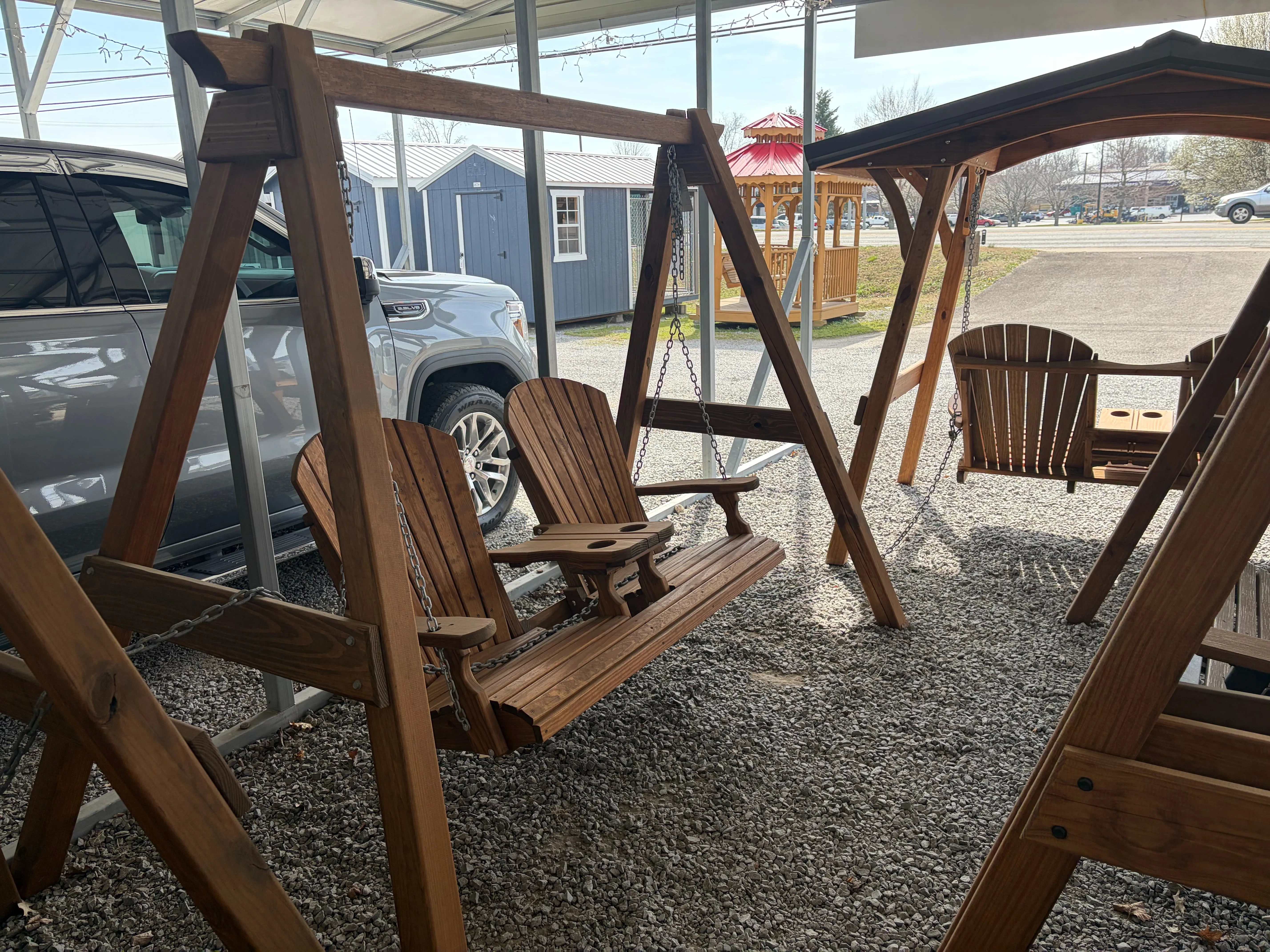 a wooden a-frame structure holding up a wood stained and sealed bench swing. There is a gray pickup truck behind it.