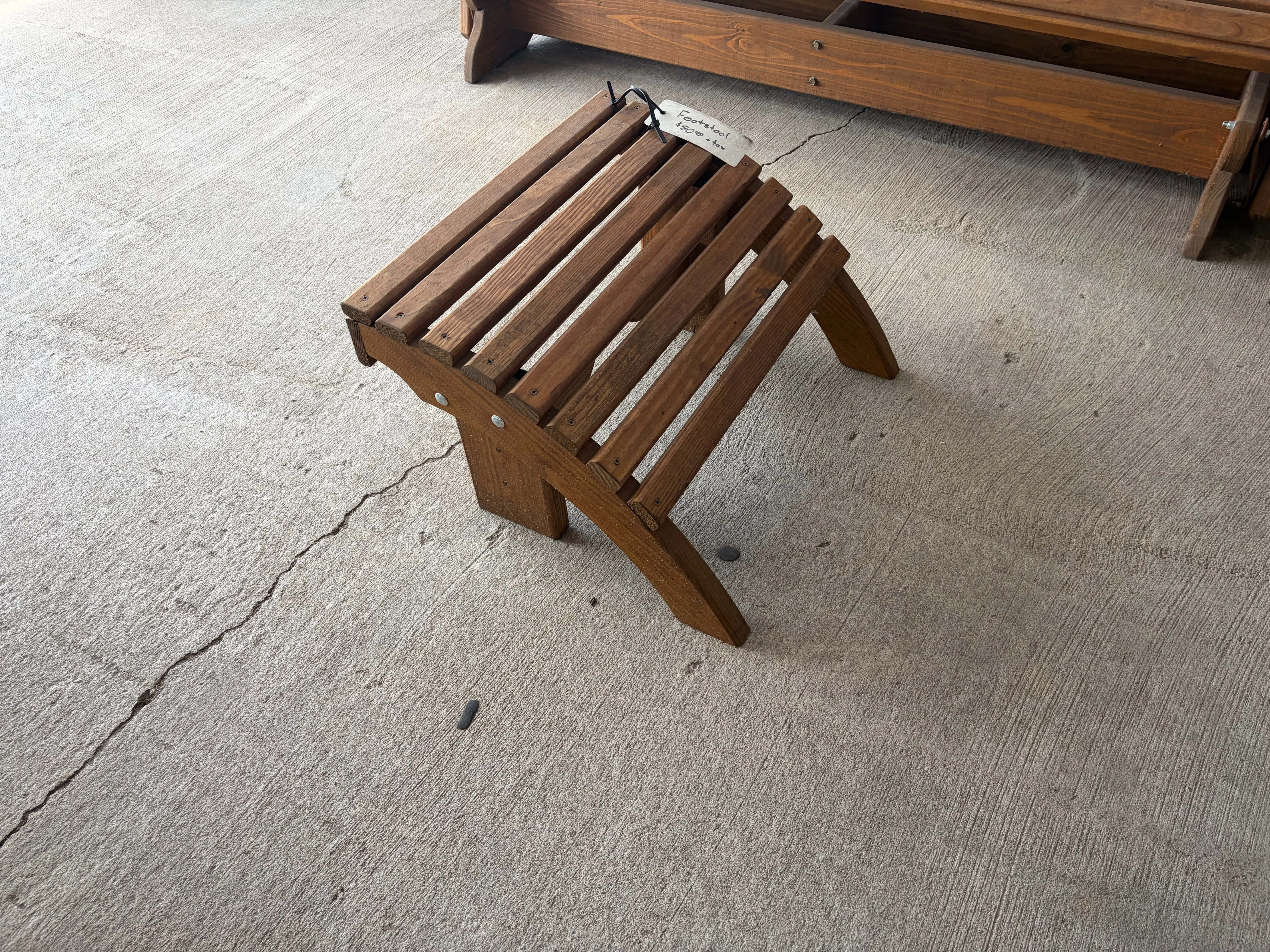 a stained and sealed wood footstool sitting on concrete. It has eight horizontal slats running across.