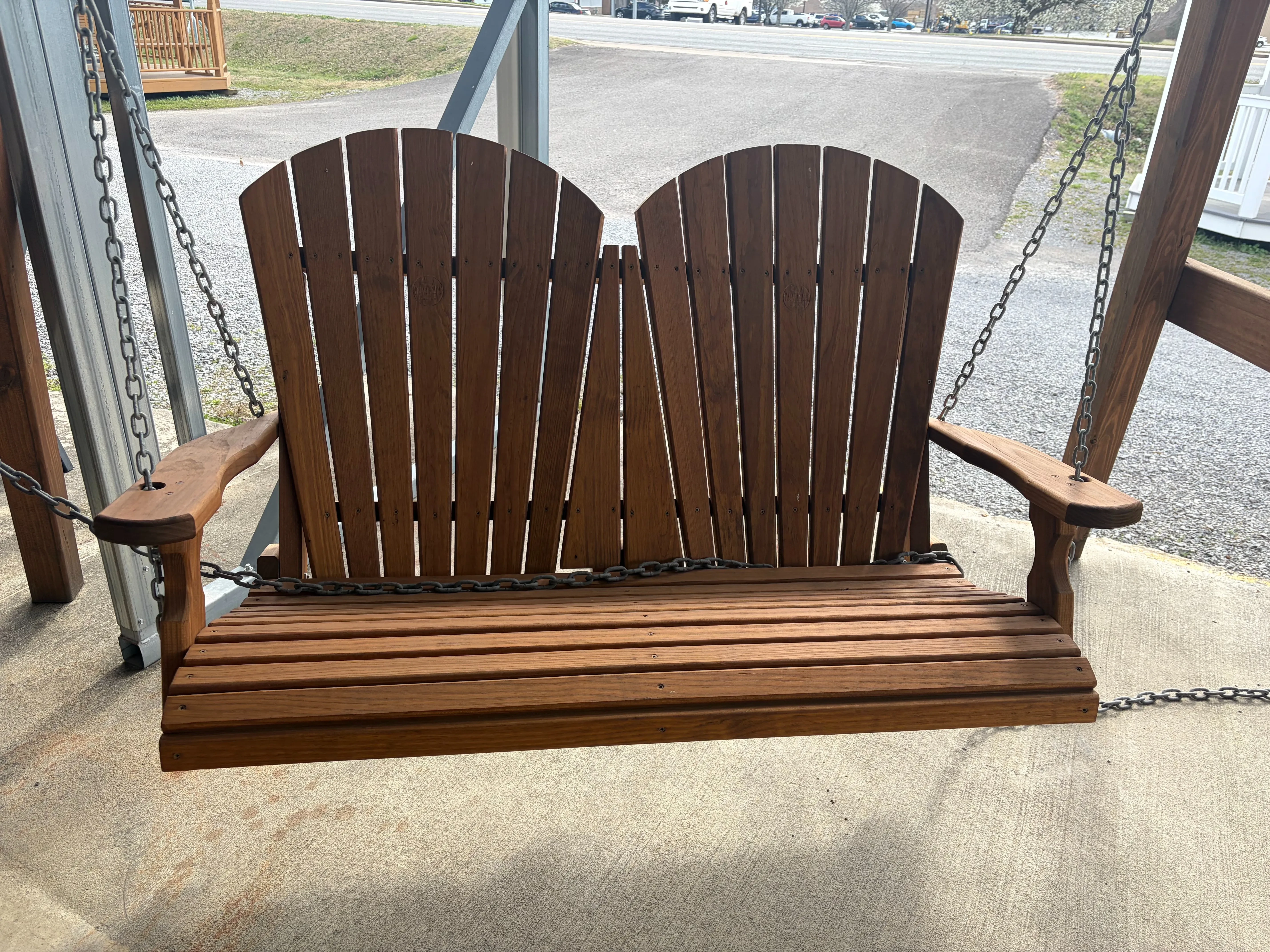 a wood stained and sealed bench swing with two seats. It is chained up and hovering above concrete