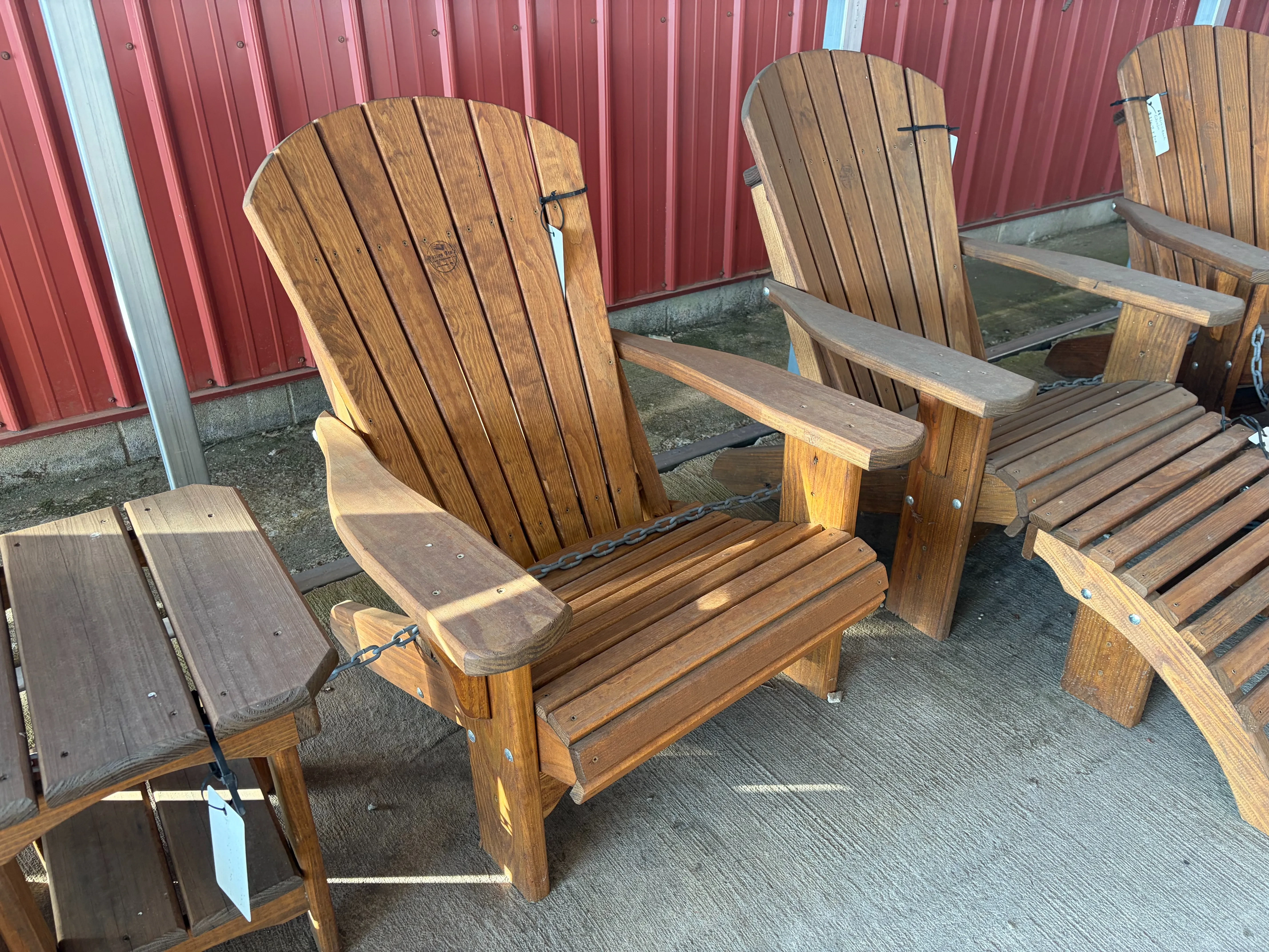 a wood stained and sealed chair sitting on concrete. It is chained up to other furniture. It has armrests