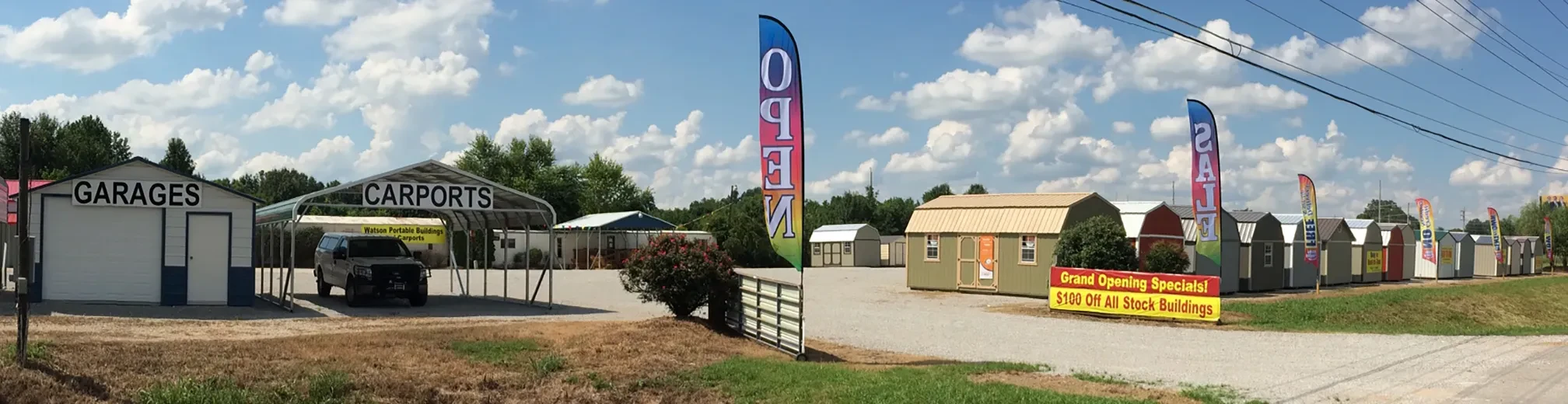 row of sheds and carports with colorful banner flags on the meridianville sales lot as seen from the road