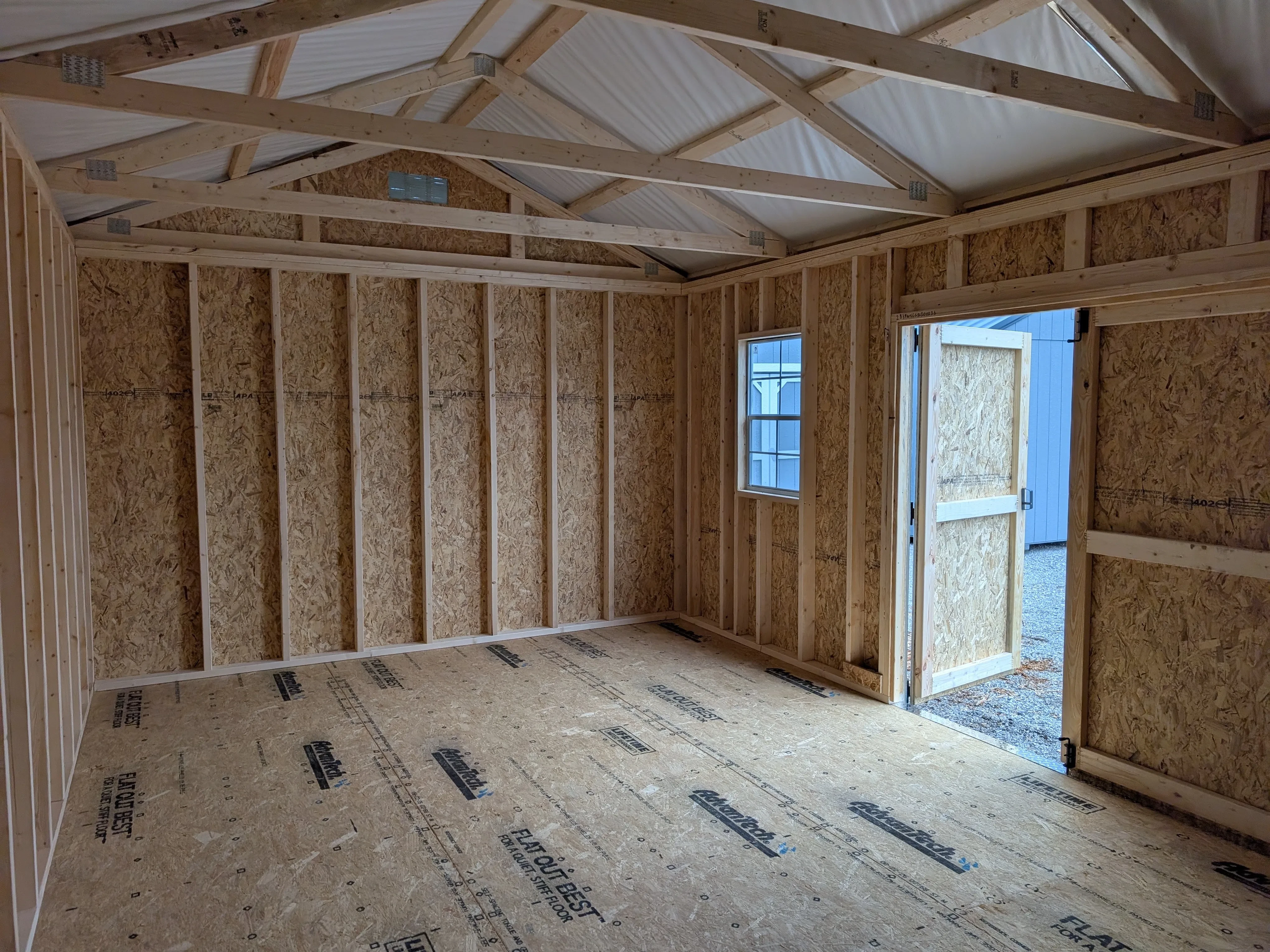 the inside of a wood garden shed looking at the right and front wall. One of the double doors is open and there is a window