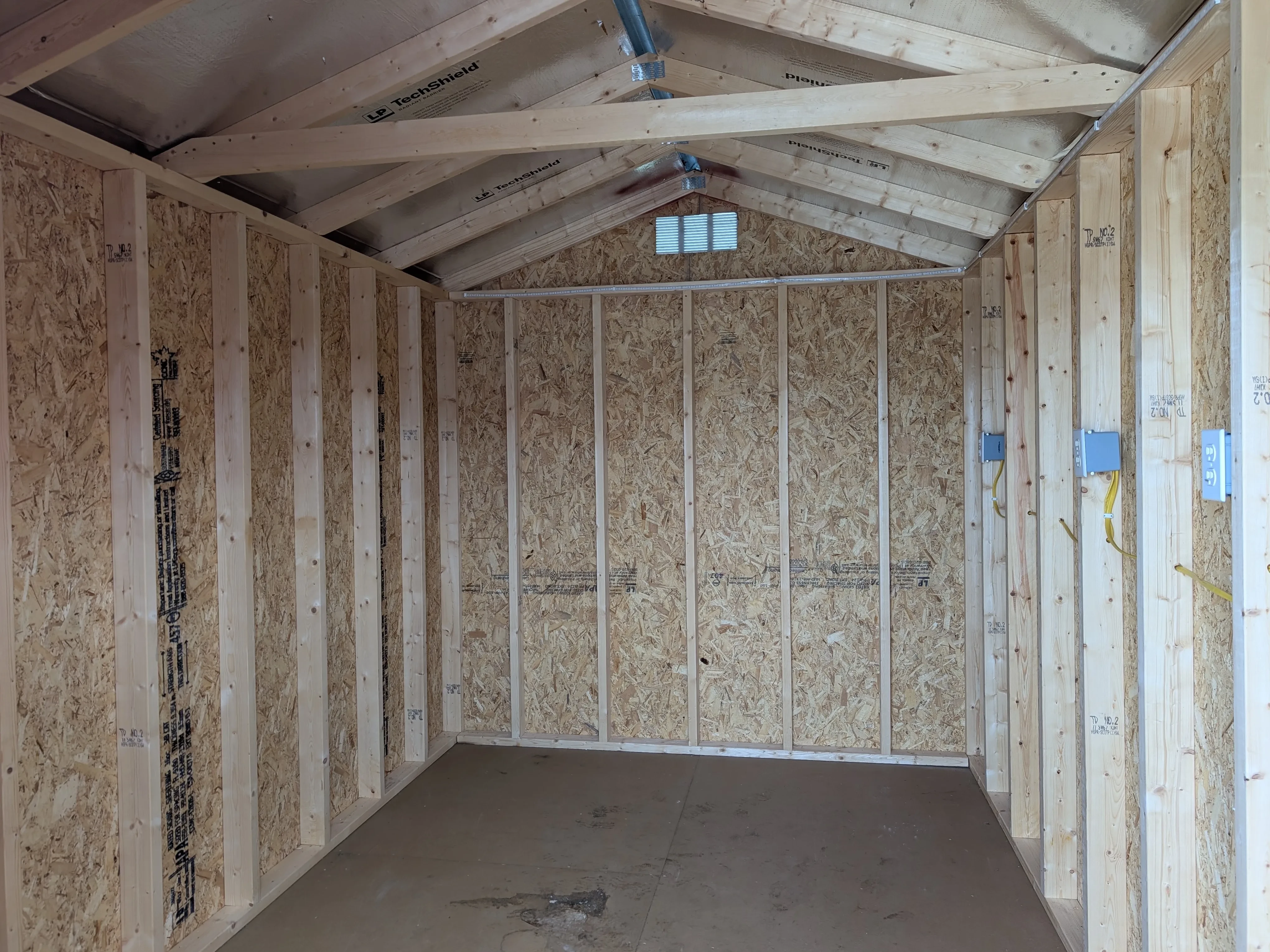 the inside of a wood utility shed. It has a vent up top. It has a solid floor and there are receptacles in the wall