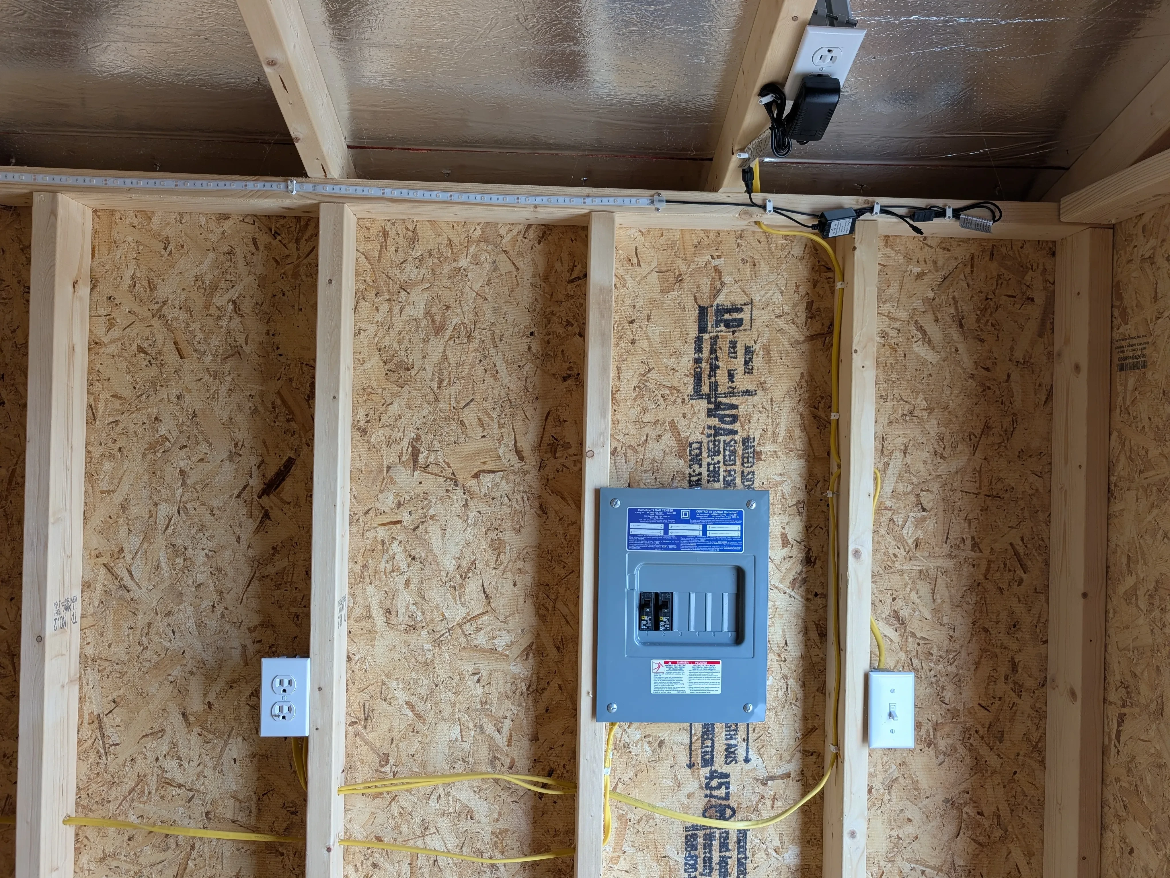 inside a wood shed looking at the wall. There is a sub-panel box with electrical wiring. There are switches and receptacles