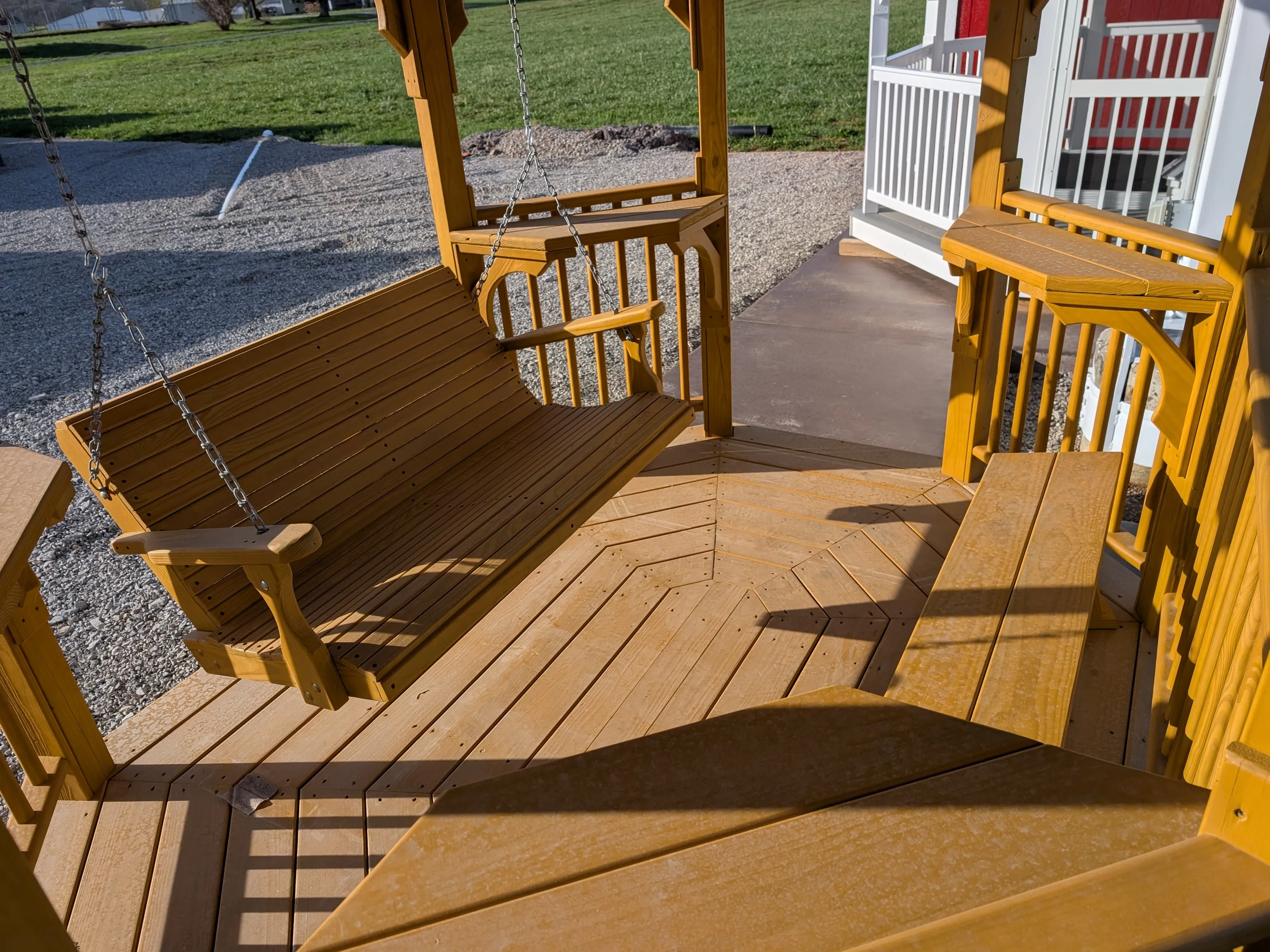 the inside of a stained and sealed teahouse. It has a bench on the right and a swing on the left. Everything is honey gold