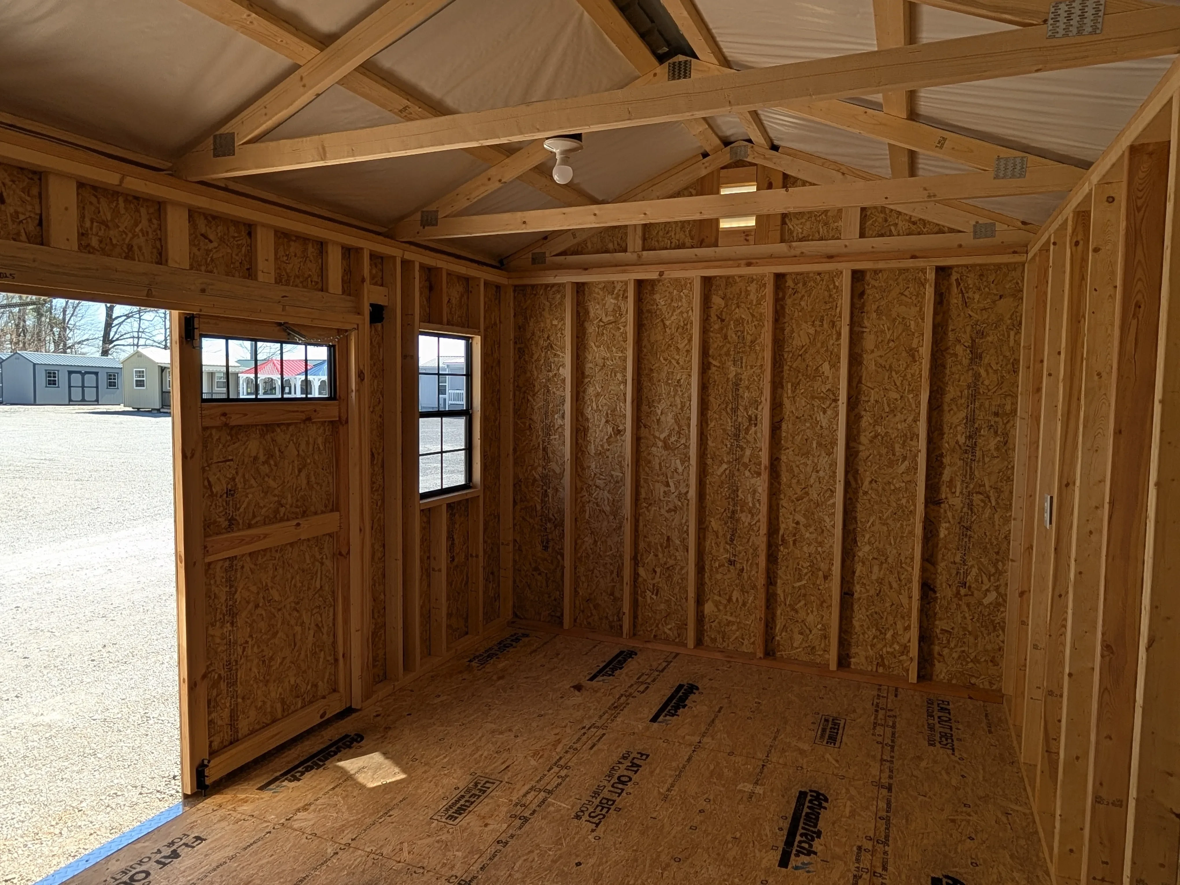 inside a wood garden shed looking at the left and front walls. There is a 2x3 window on the front wall and a transom window