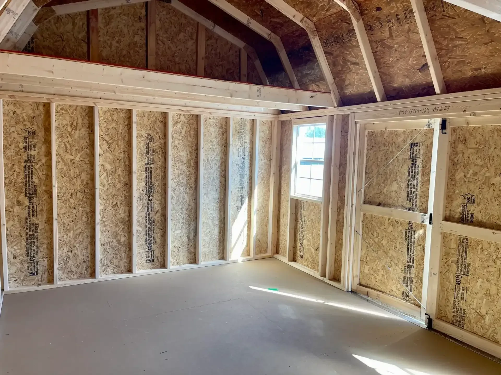 The inside of a side lofted barn showing the loft, a window, and double doors open
