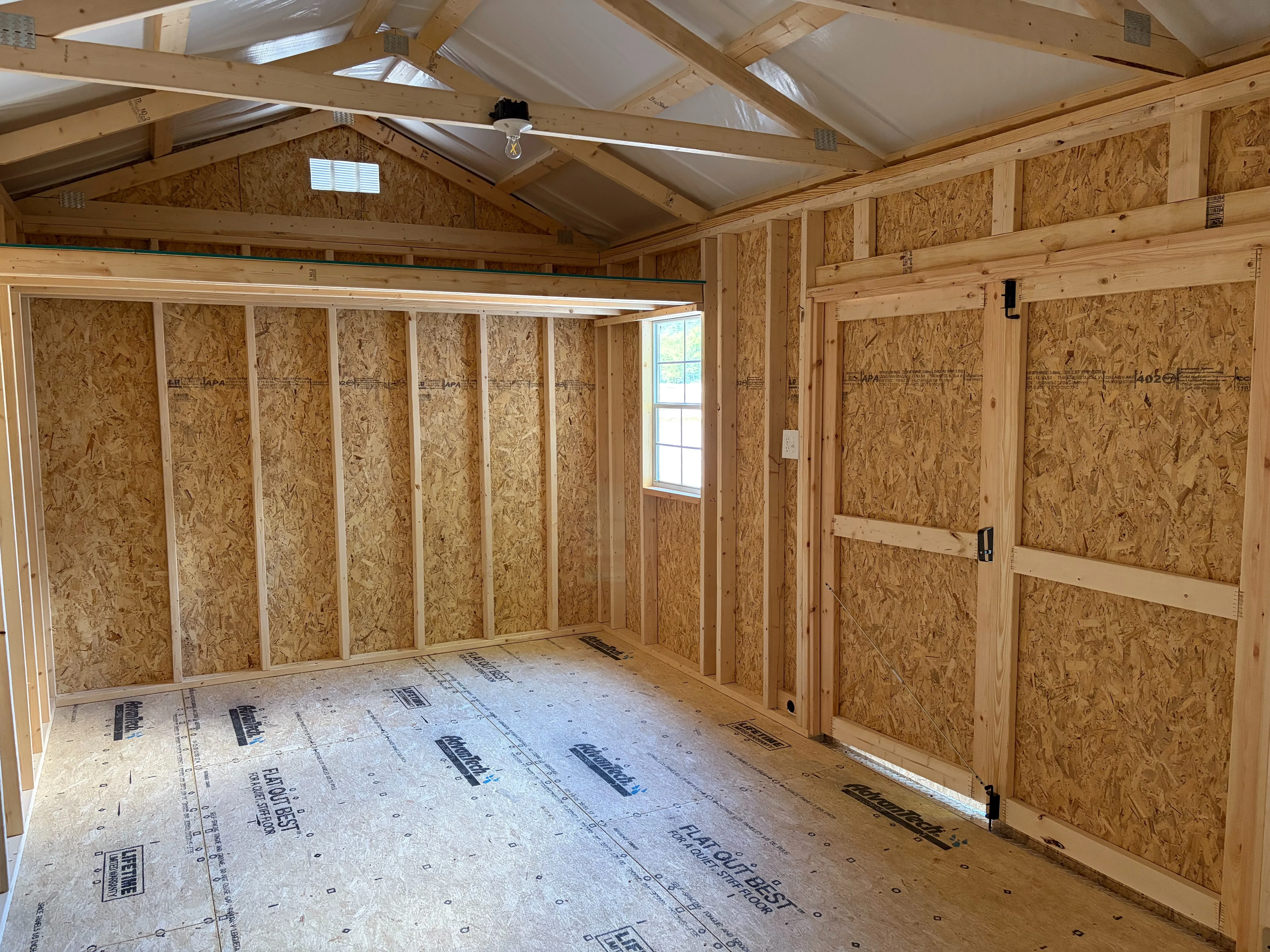 the left interior of a wood garden shed which has a window on the front wall with electrical package and loft