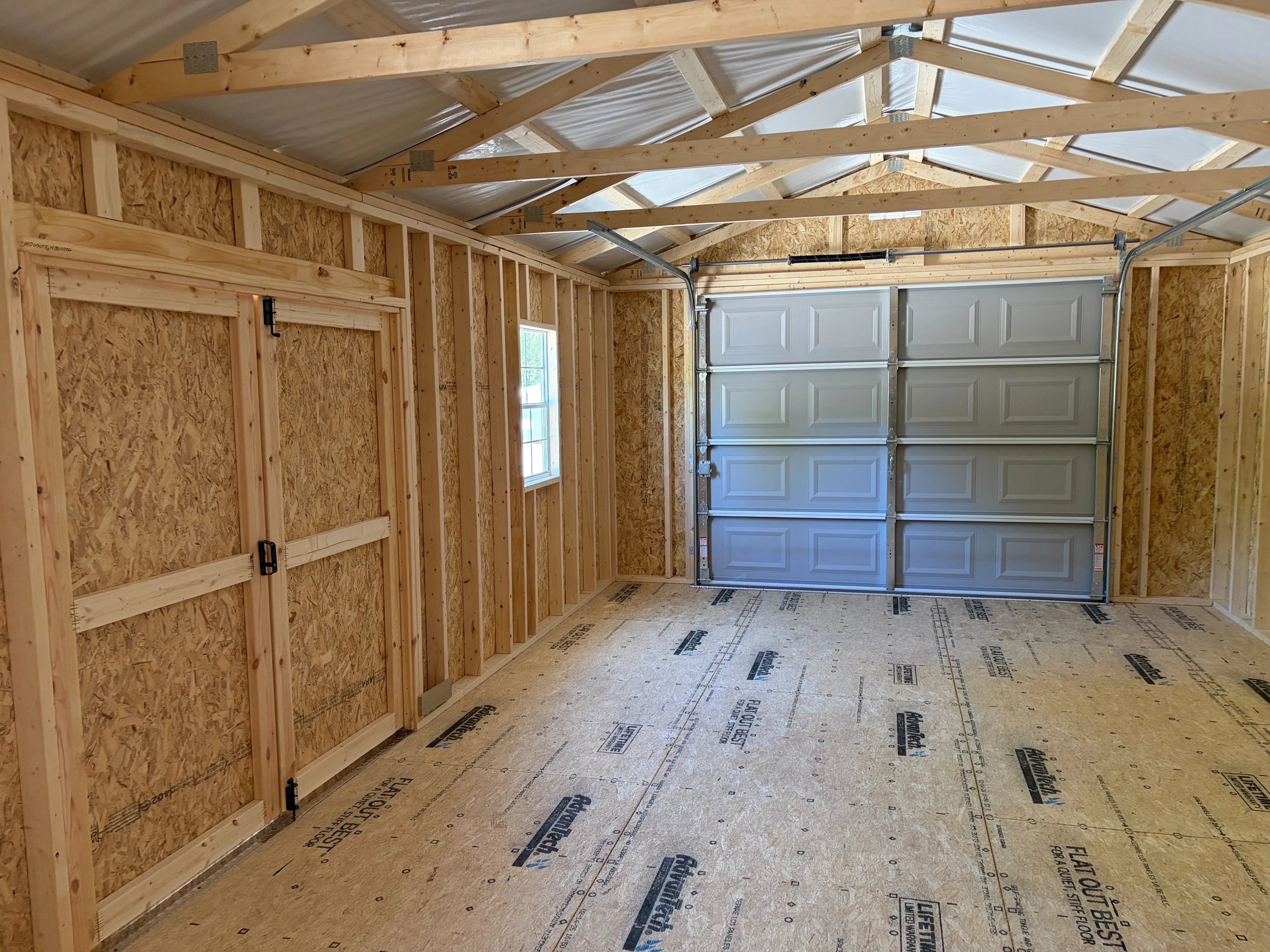 inside a large garage shed with overhead garage door, multiple windows, a loft, and double doors that are closed