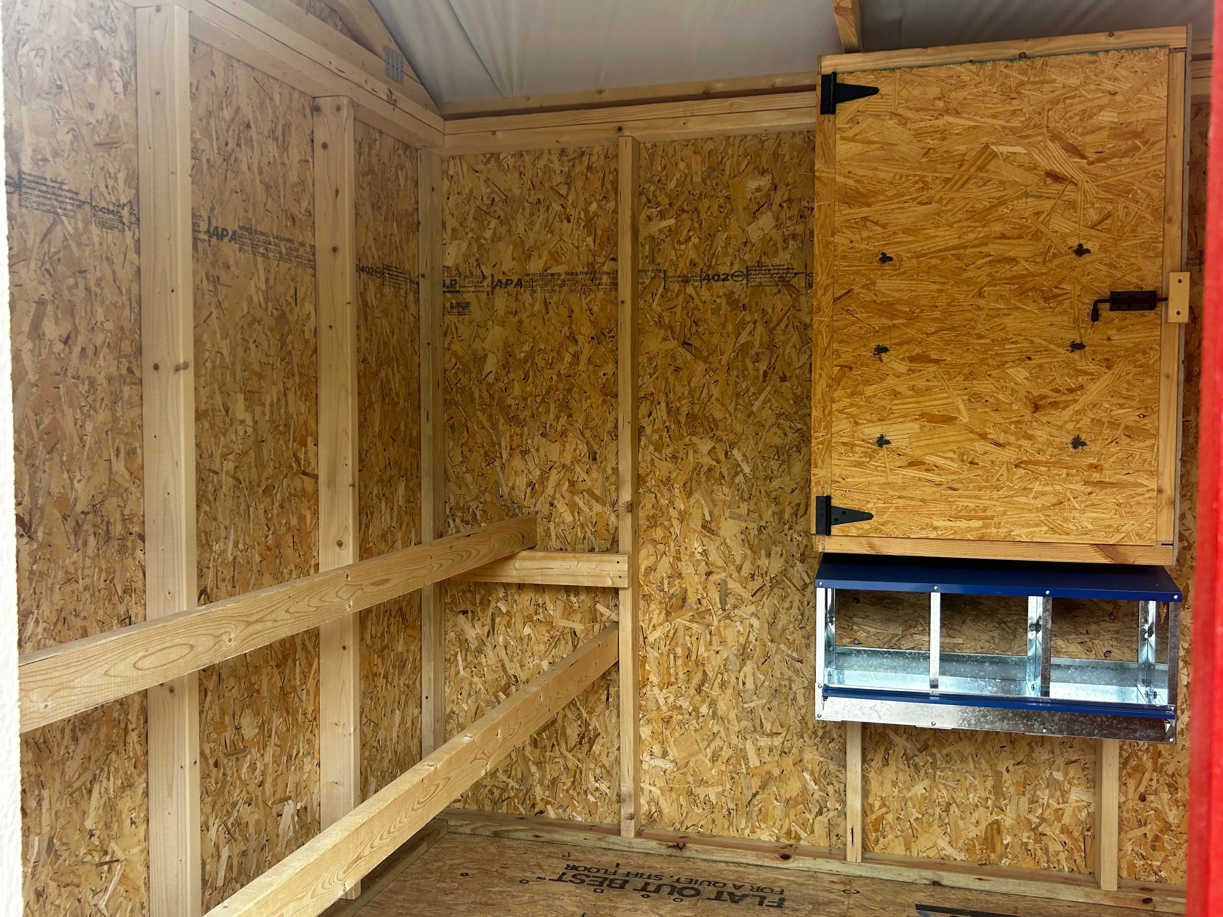 Inside of a chicken coop showing nest boxes, cabinet and and 2 roosts
