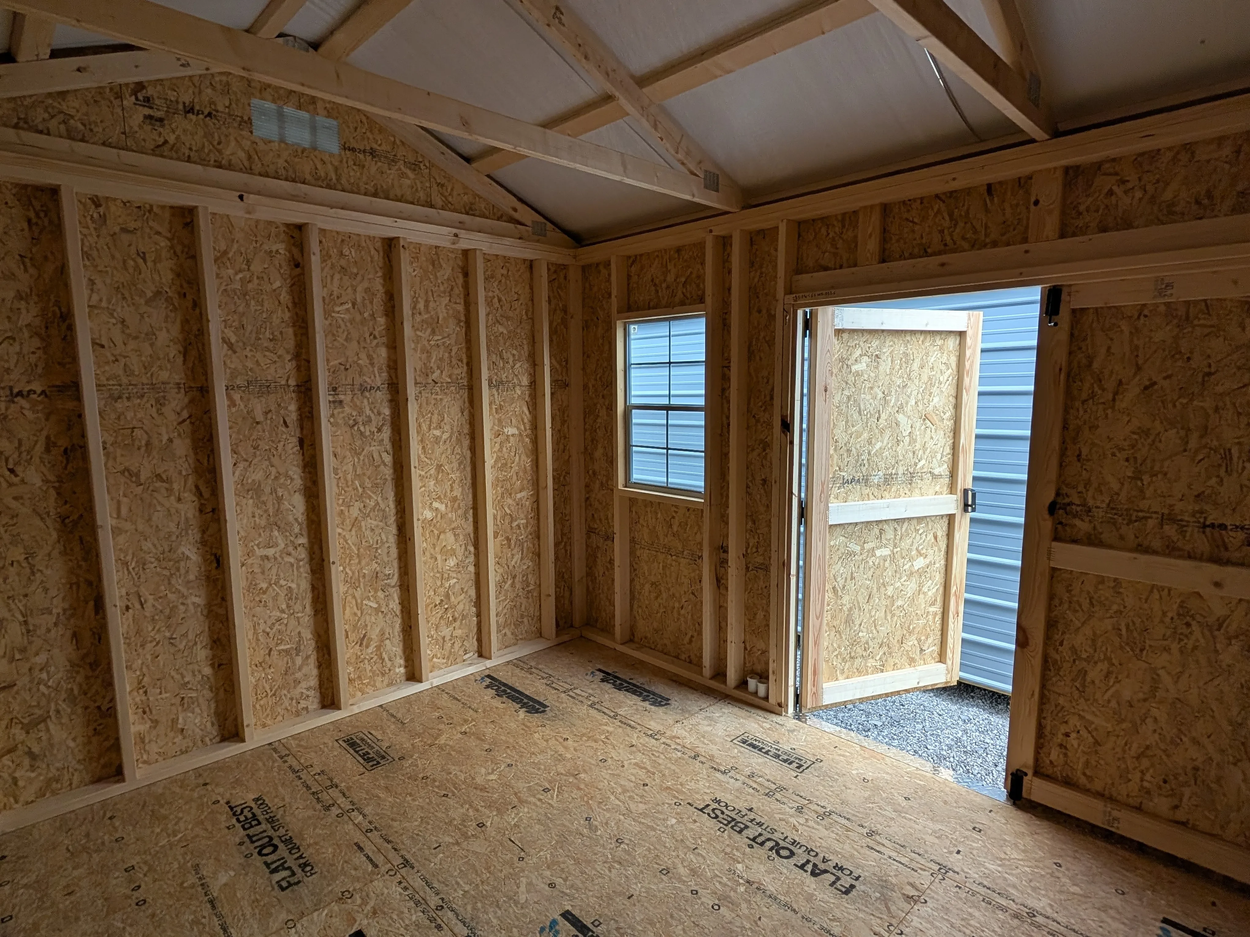 inside a wood garden shed looking towards to double doors which are open. There is a window next to the doors.