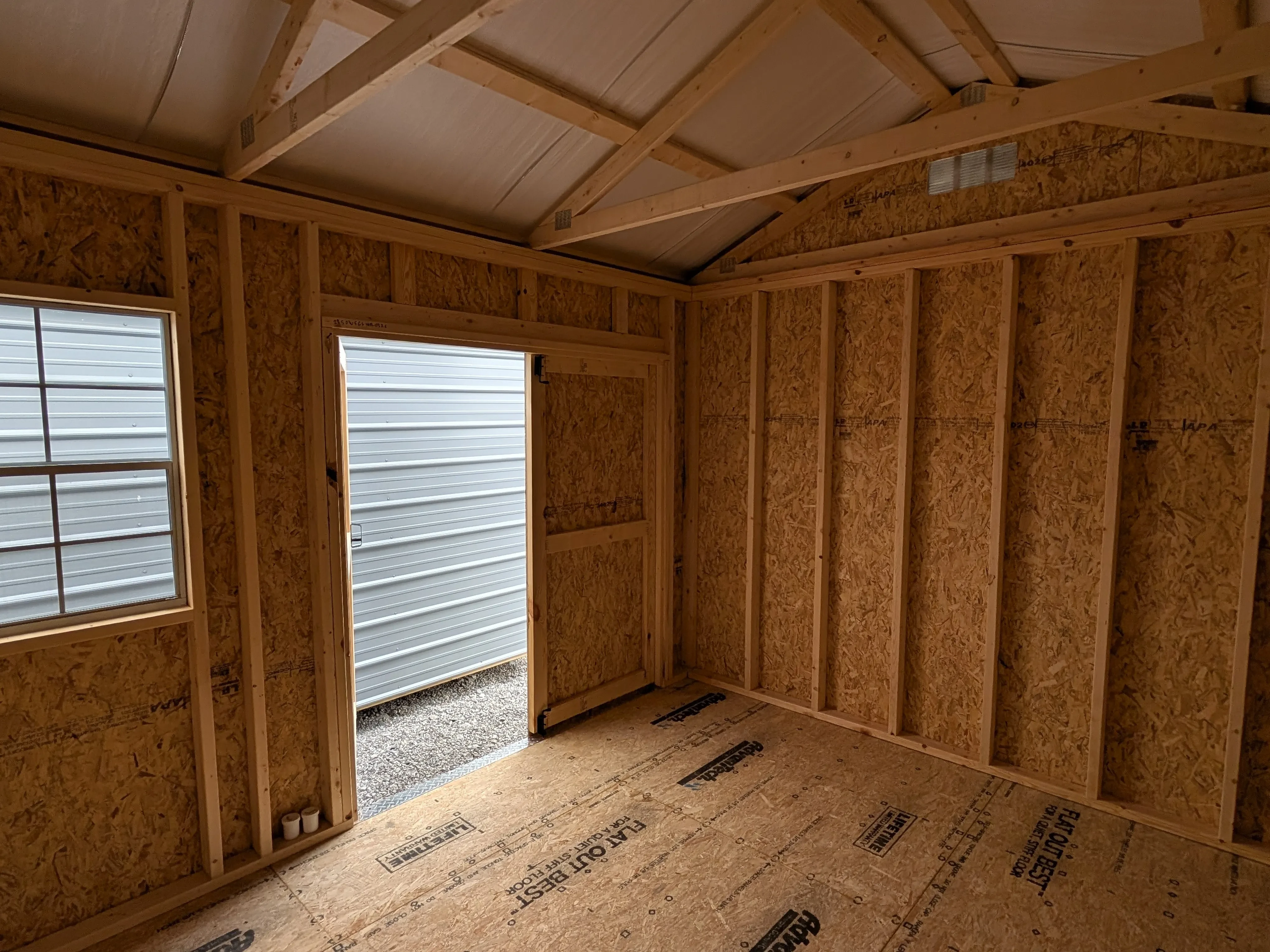inside a wood garden shed looking towards the corner. You can see the door open and a window next to it.