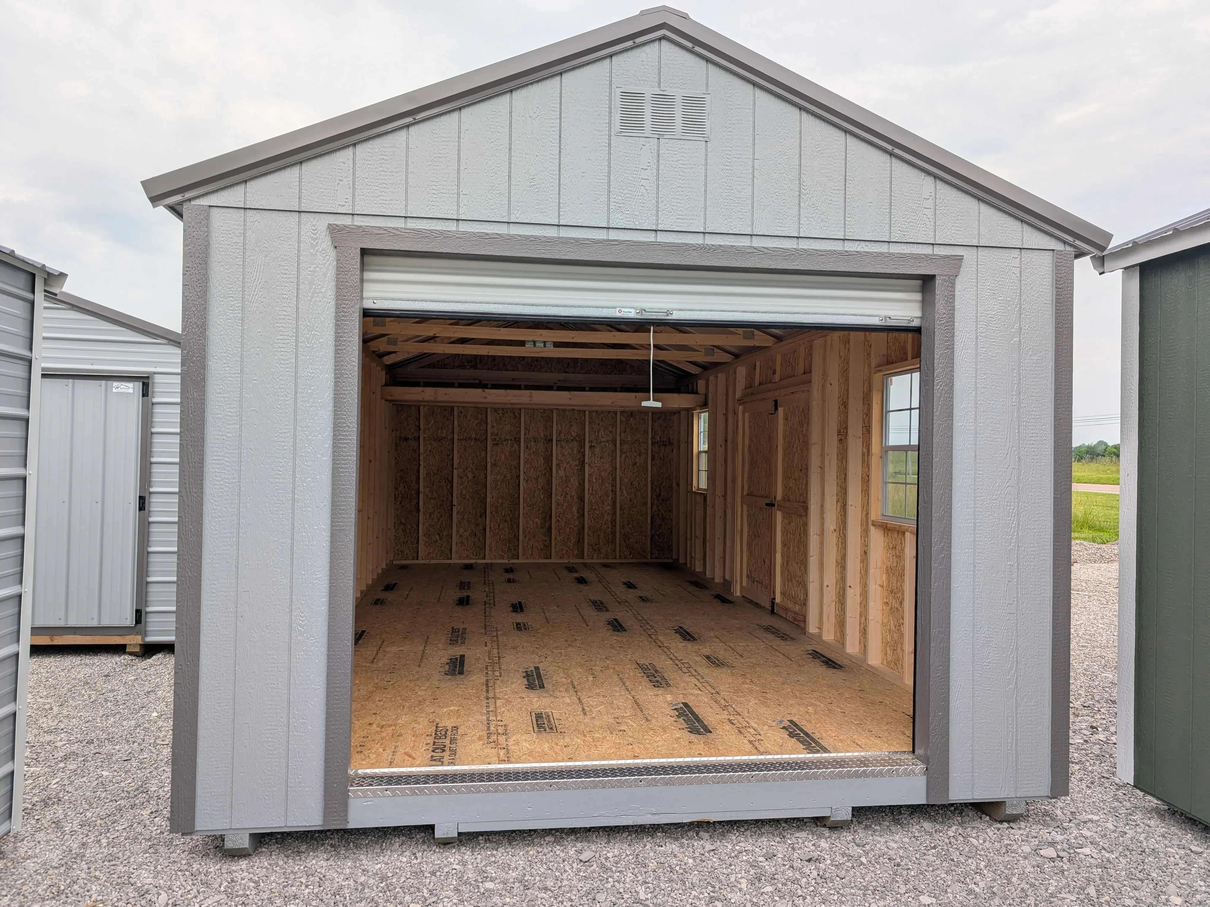 a large portable wooden garage with the garage door open. Inside there are windows and a loft