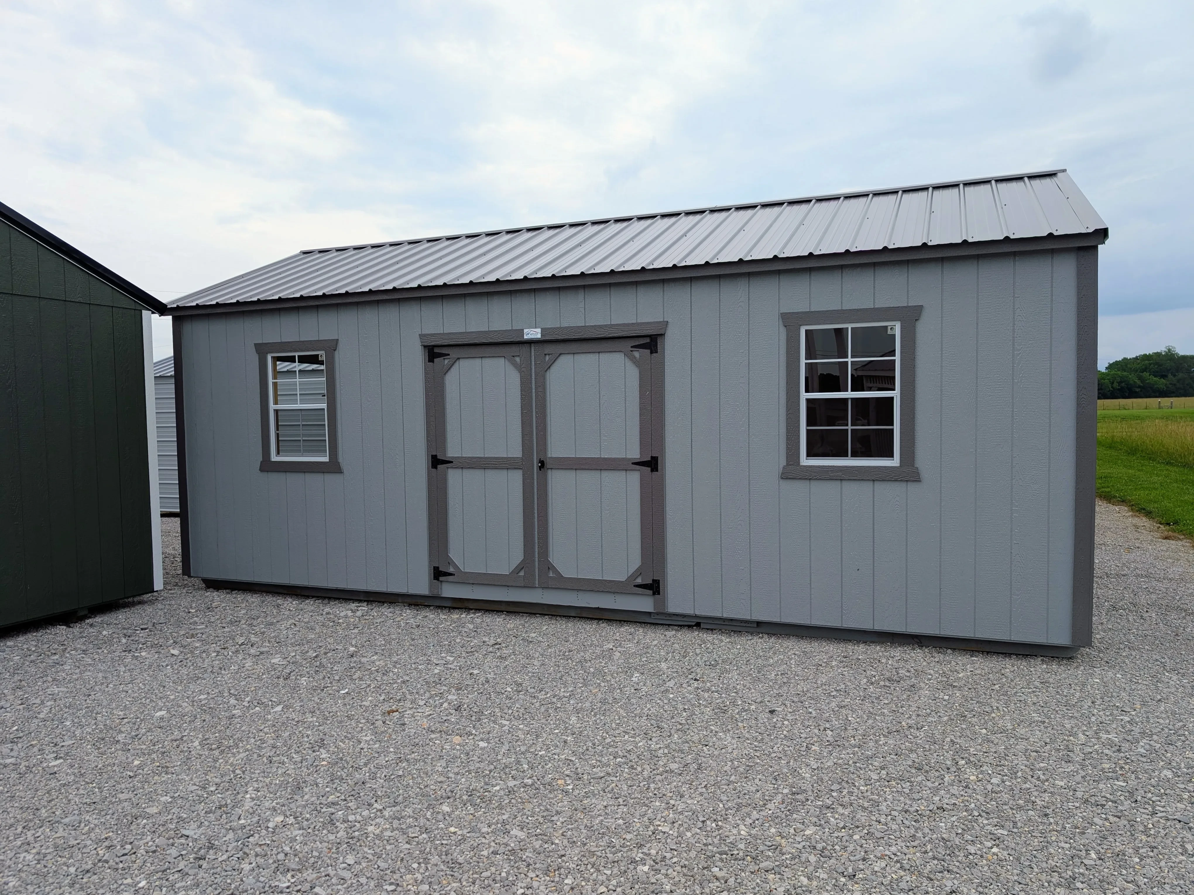 the outside of a portable wooden garage. It has double doors and a 2x3 window on each side of them.