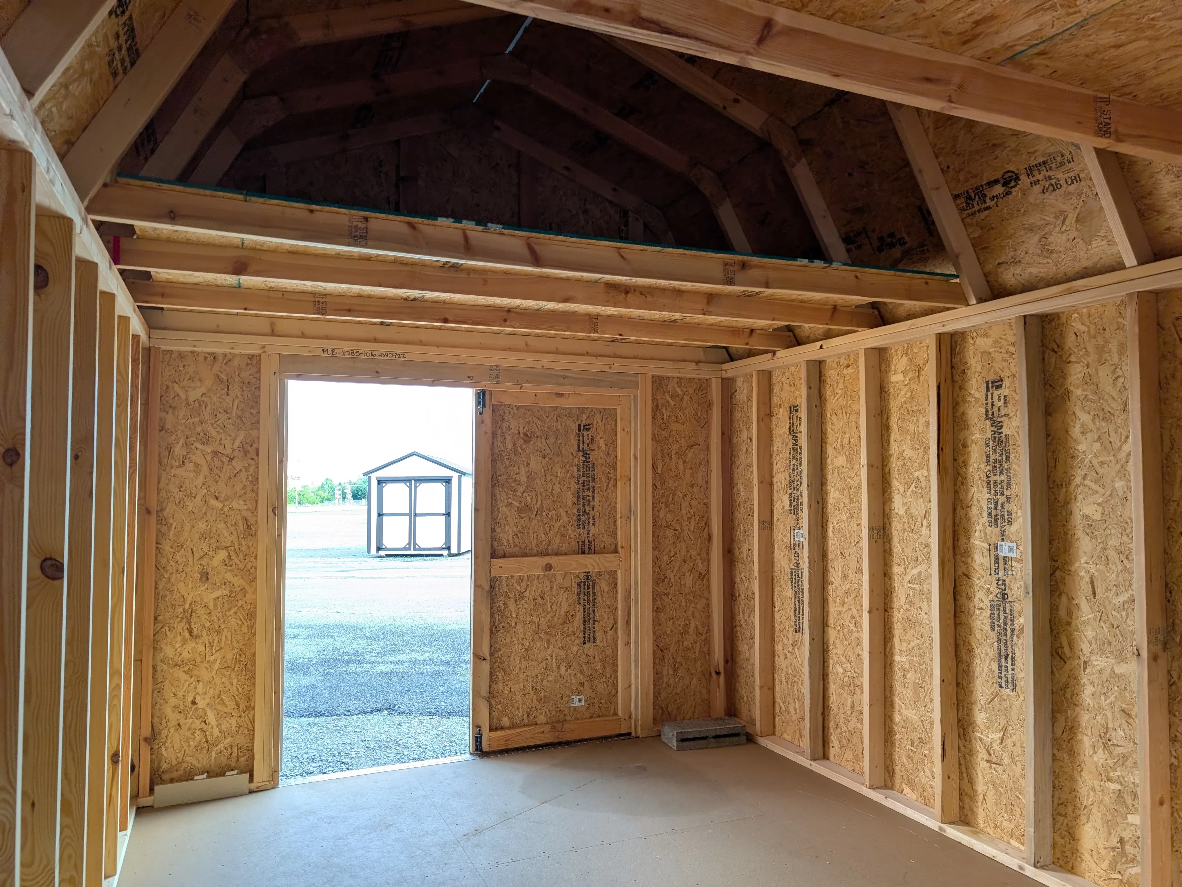 inside a wood lofted barn looking at the front wall. There are double doors with one door open, and a loft above the doors