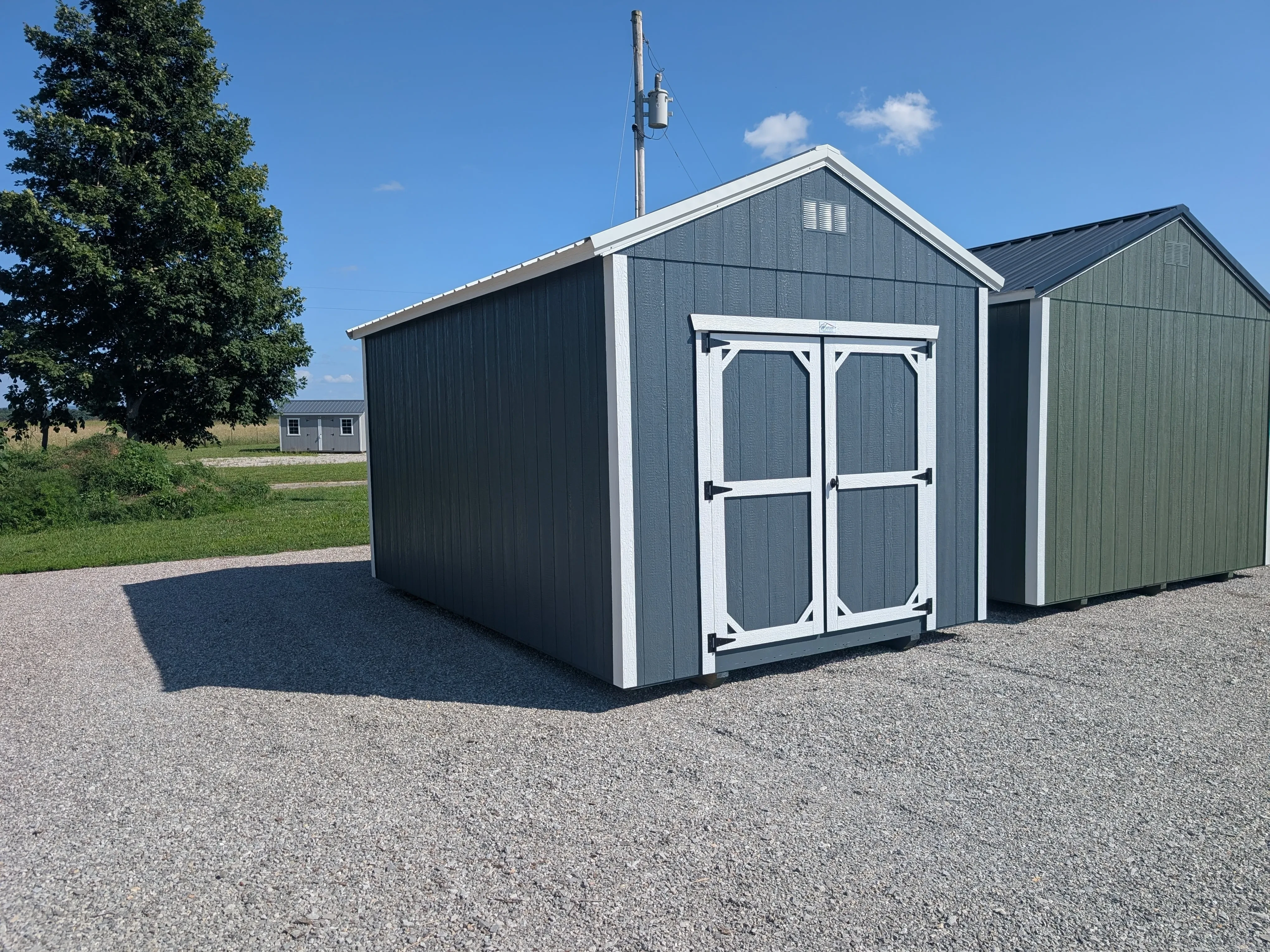 a blue wood utility shed with double doors and white trim. It is next to a green shed with white trim
