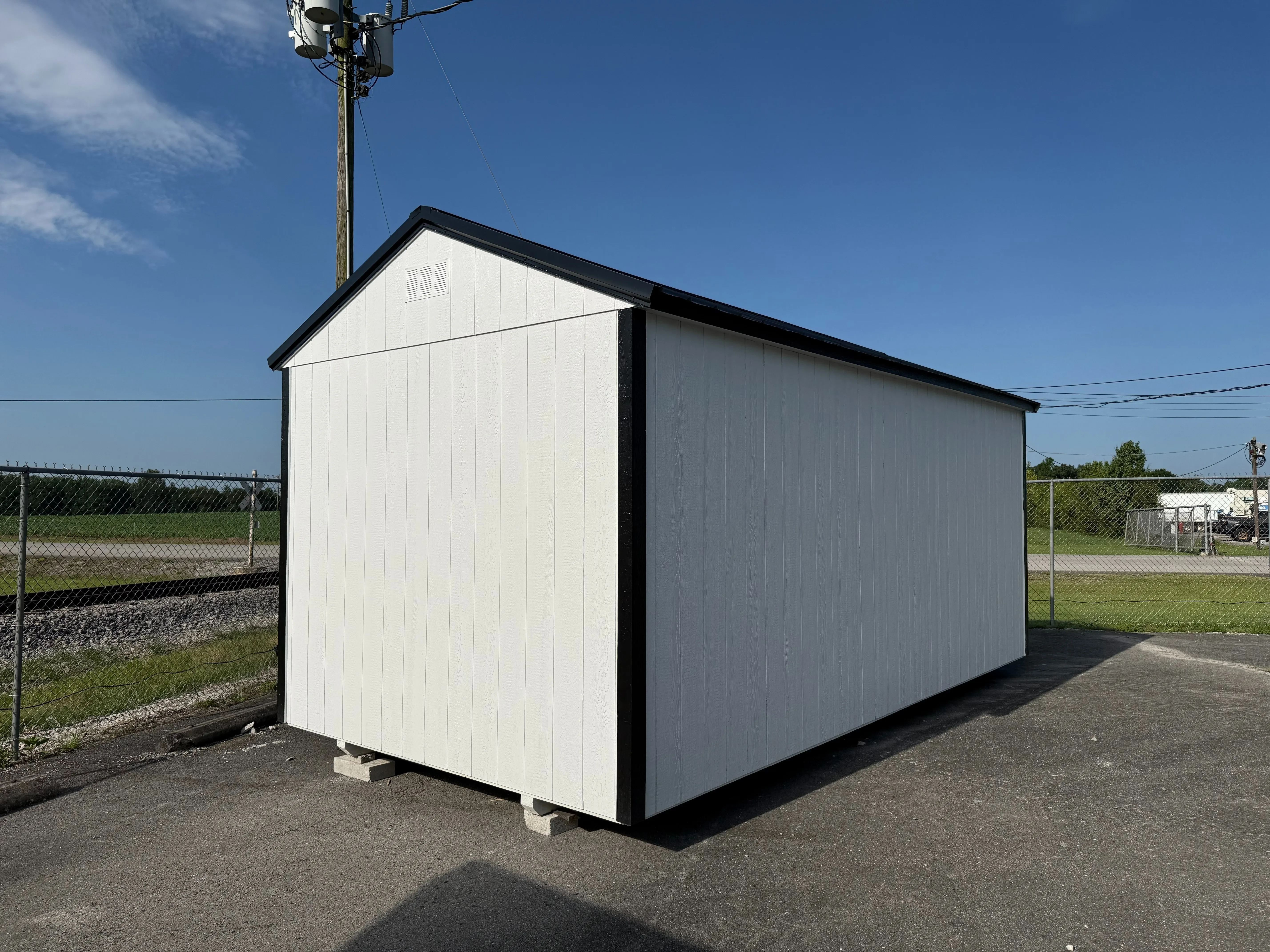 looking at the back left corner of a white garden shed. It has black trim and a black metal roof