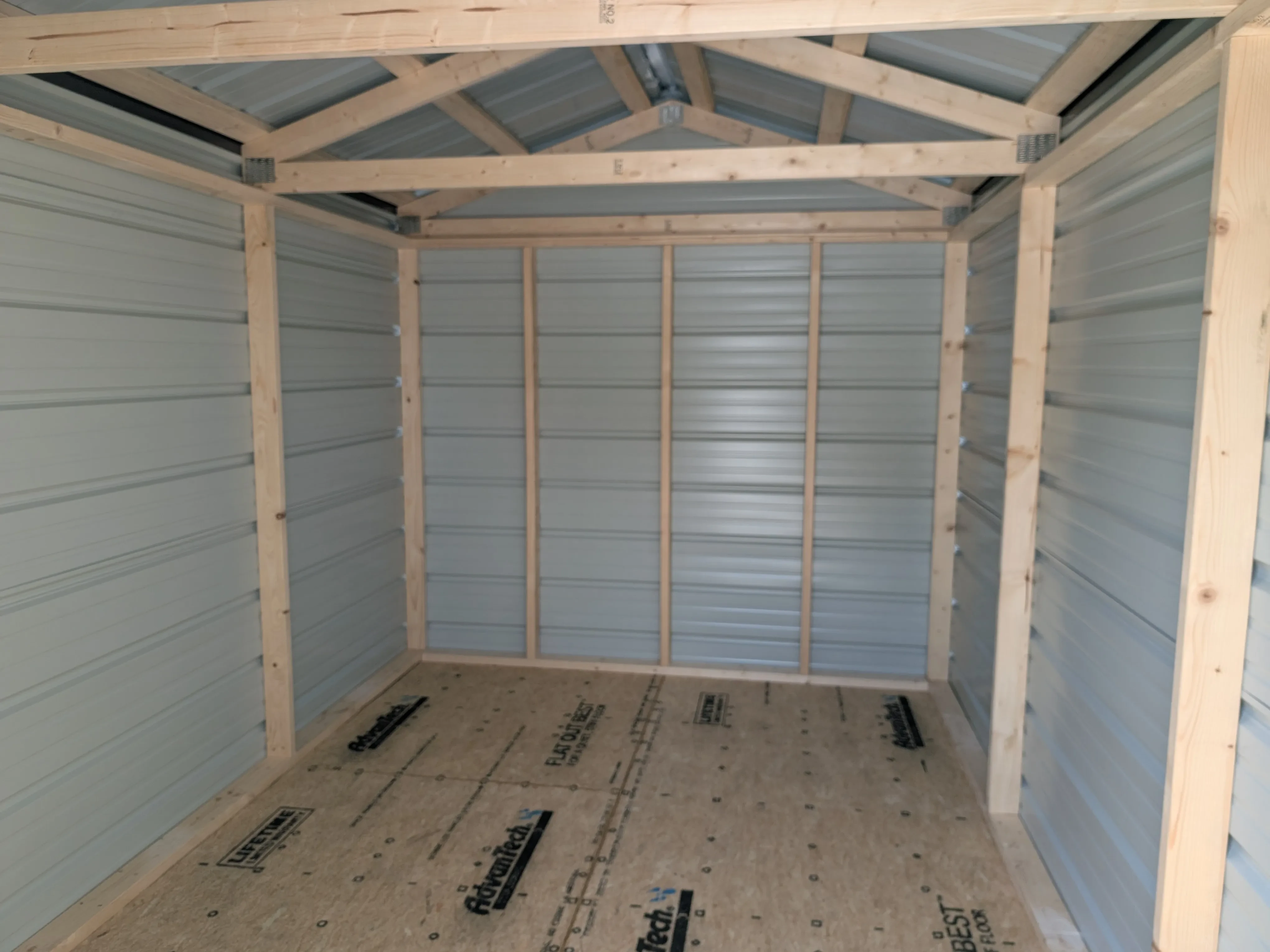 inside a metal utility shed looking at the back wall. You can see the lumber framing and the floor