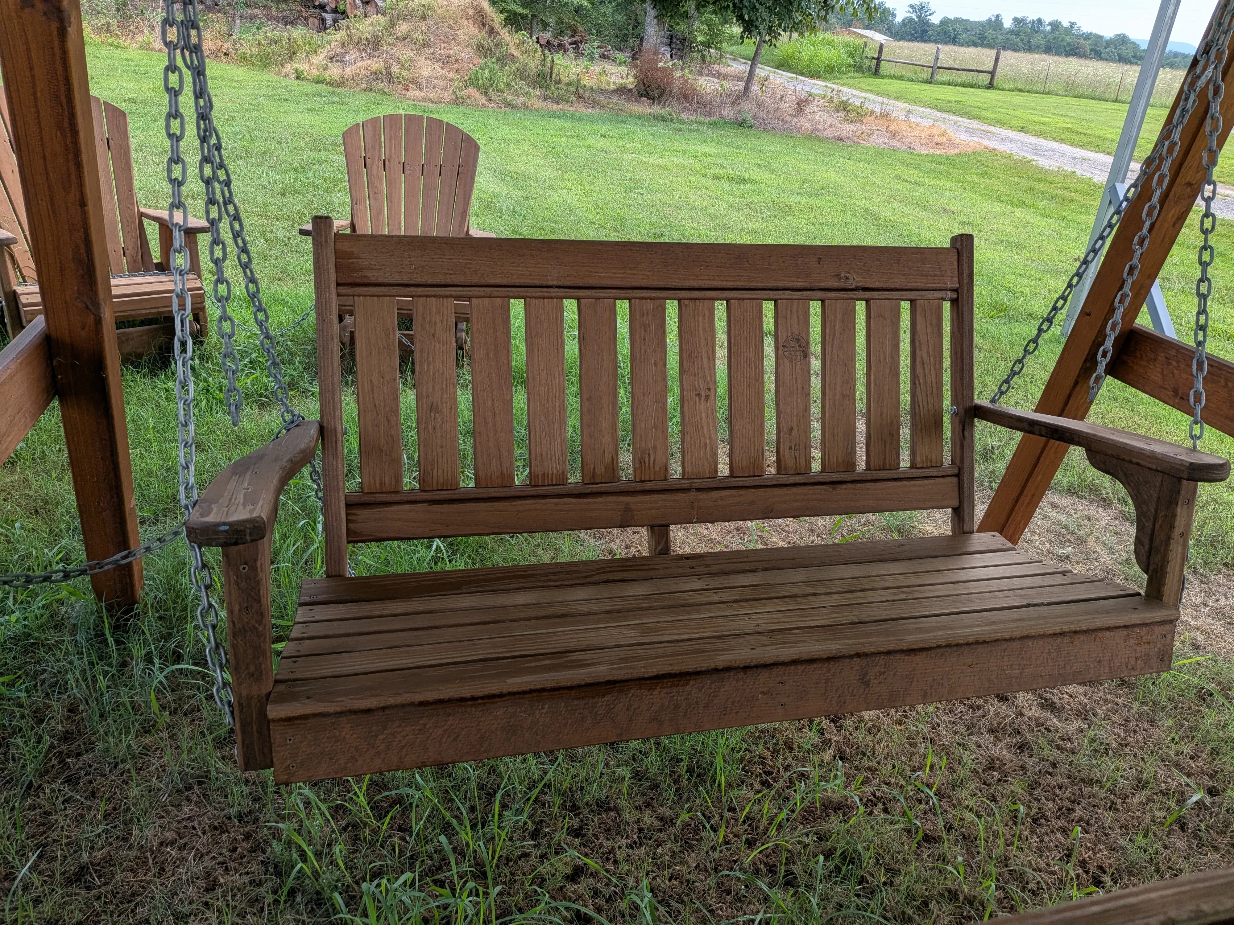 a wood garden swing hovering above grass. It is professionally stained and sealed a dark brown