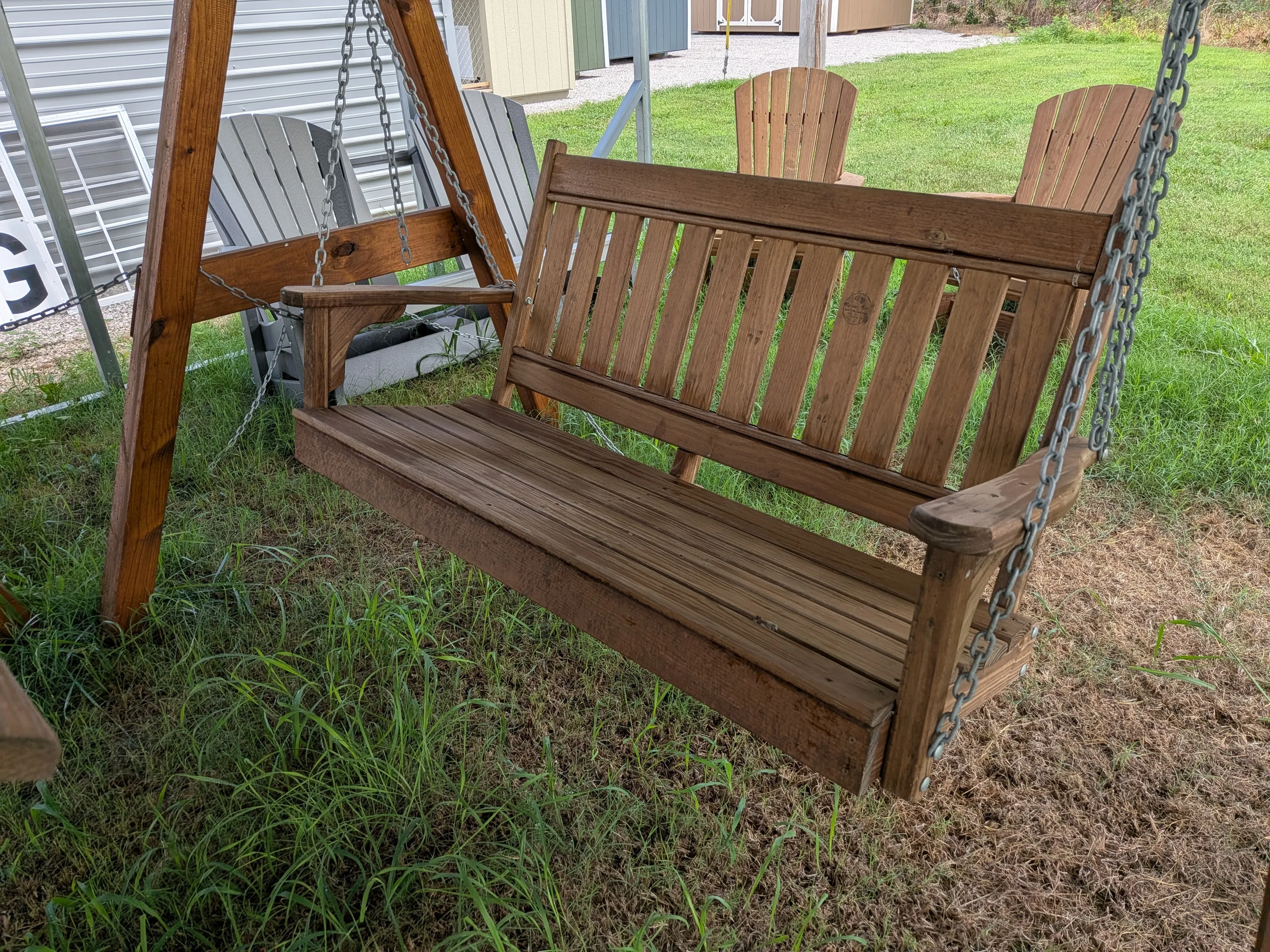 a dark brown wood stained and sealed garden swing hanging by chains over some grass.
