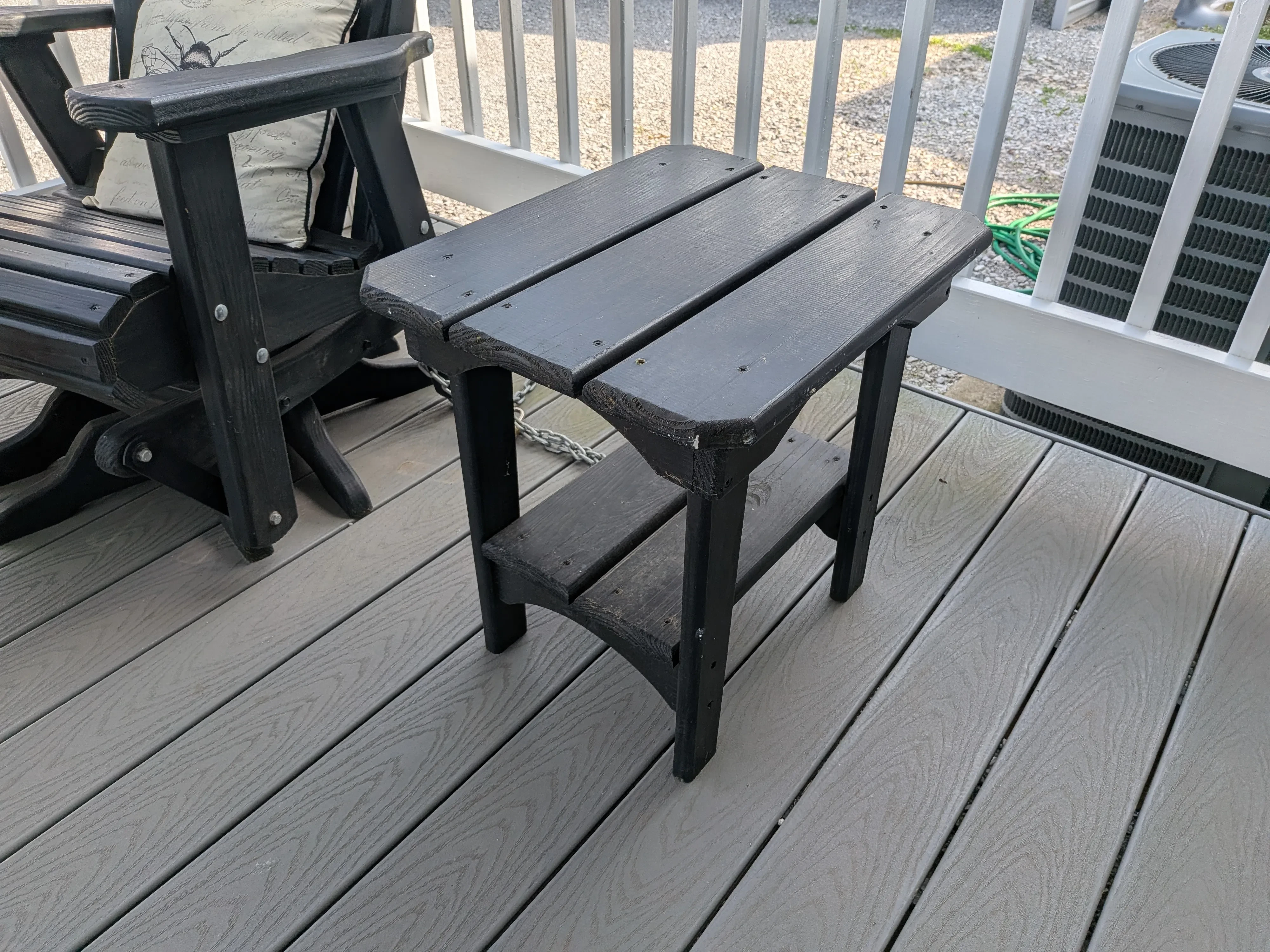 black wooden end table sitting on a porch next to a black chair