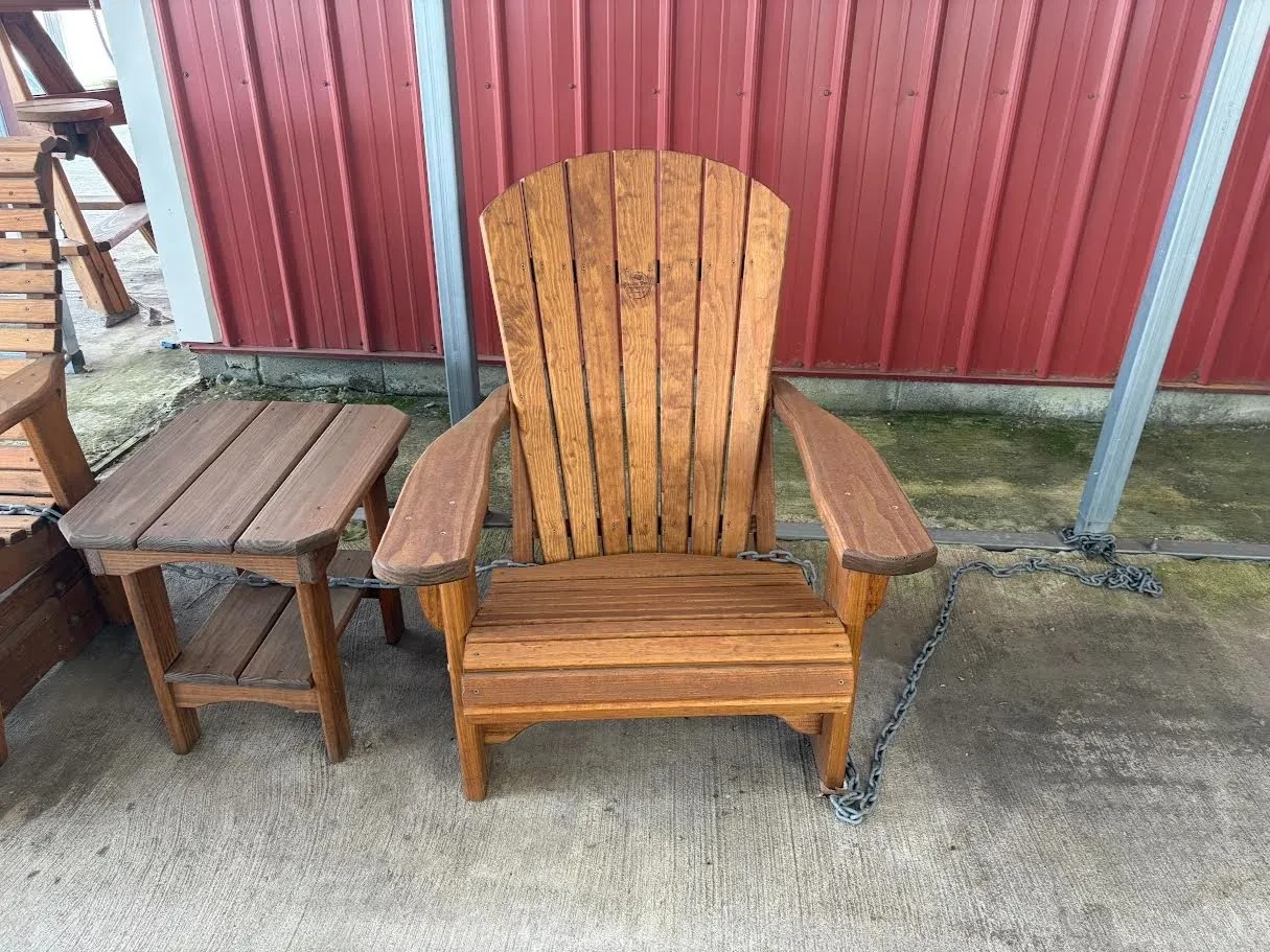 a chair sitting on concrete. It is made out of wood material. It is light brown with end table on the side