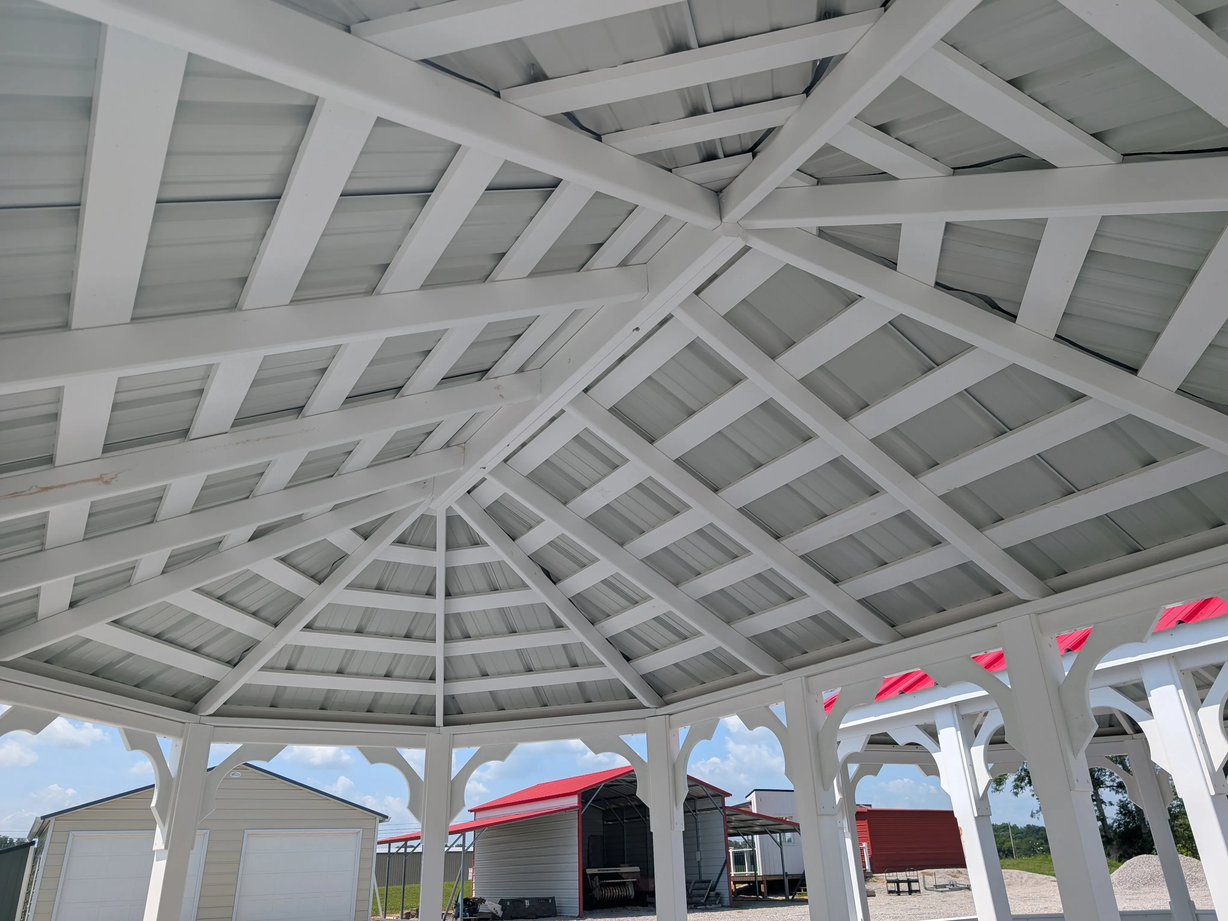 looking up at the roof of a white vinyl gazebo, you can see the posts and the bottom of the metal roof