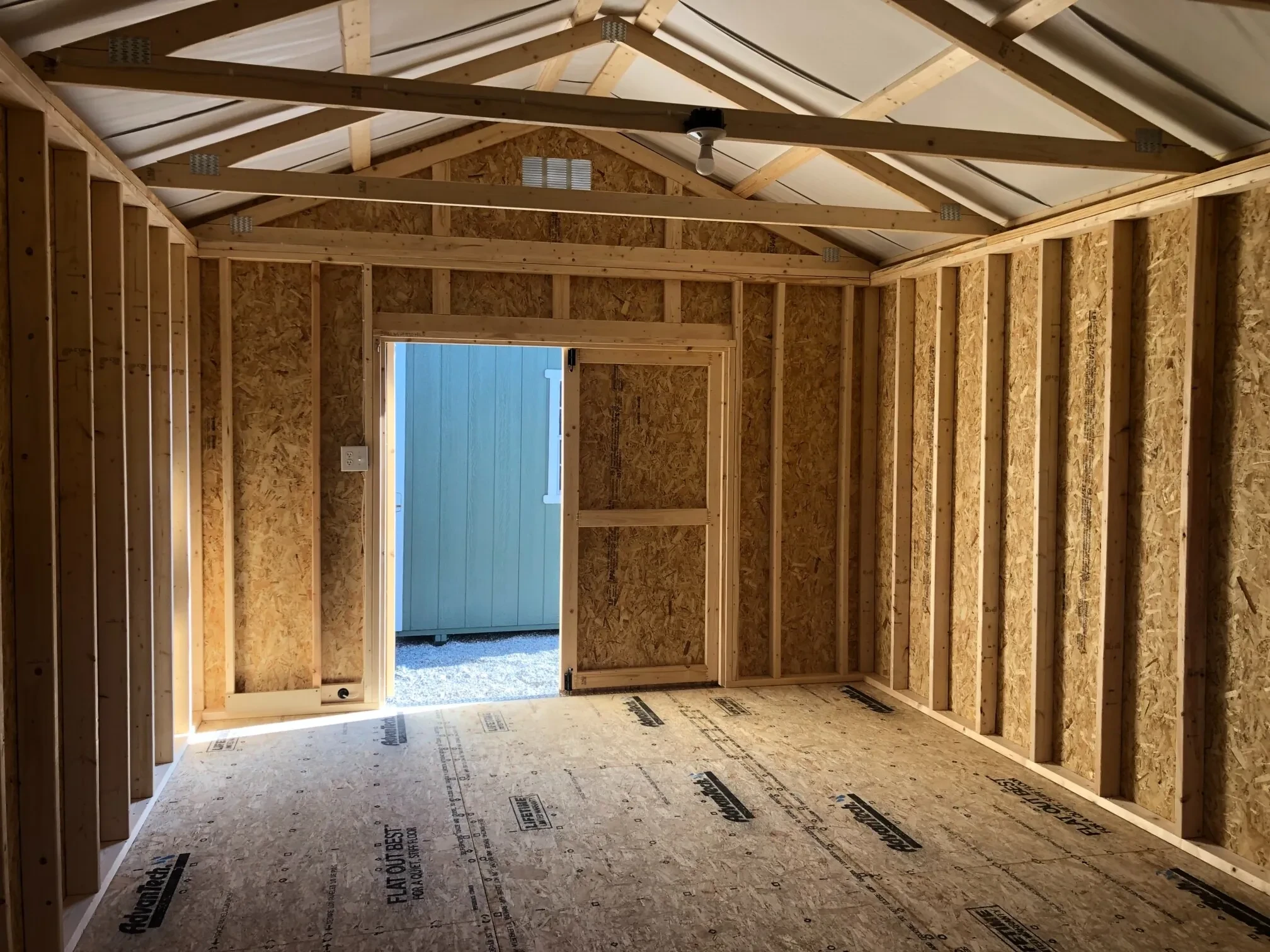 The inside of a wood shed showing the double doors open and a light bulb hanging from the roof