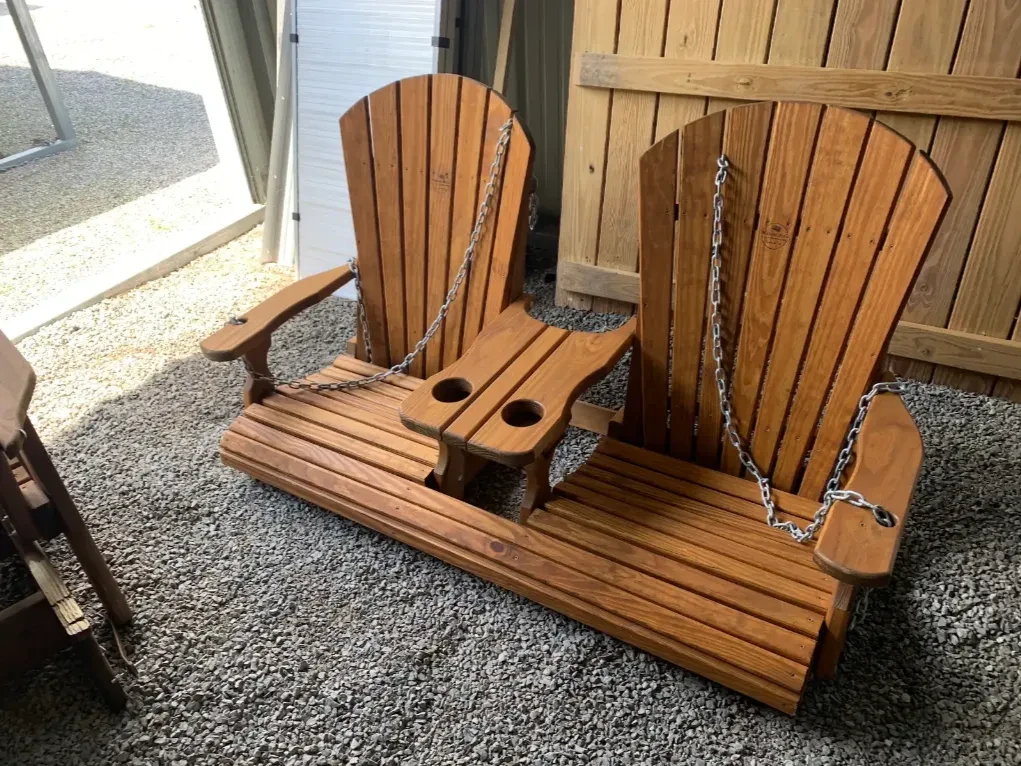 a swing sitting on gravel. It is wood stained and sealed and has a center console in the center