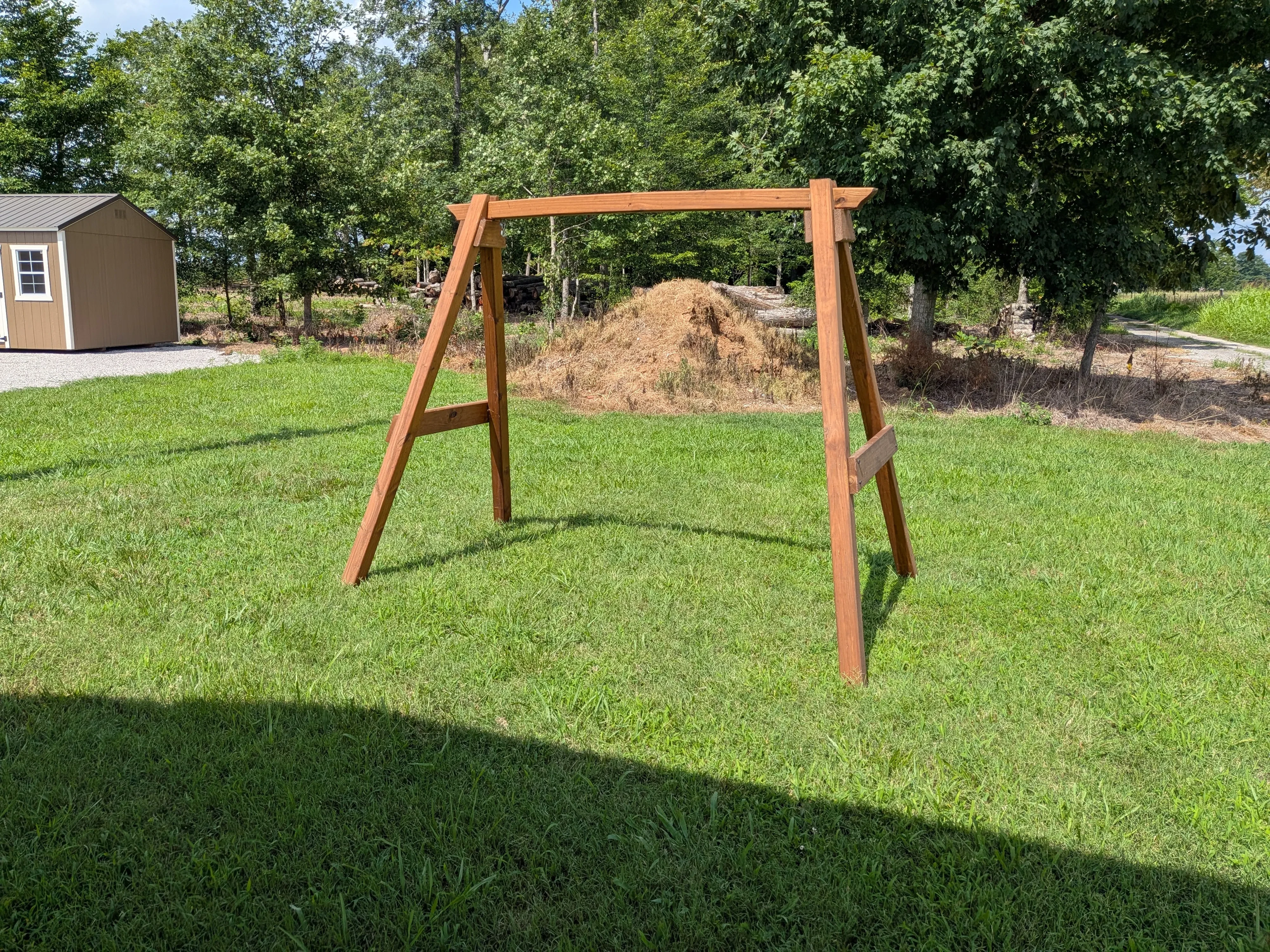 a wooden a-frame structure that is stained and sealed standing in the middle of a field.