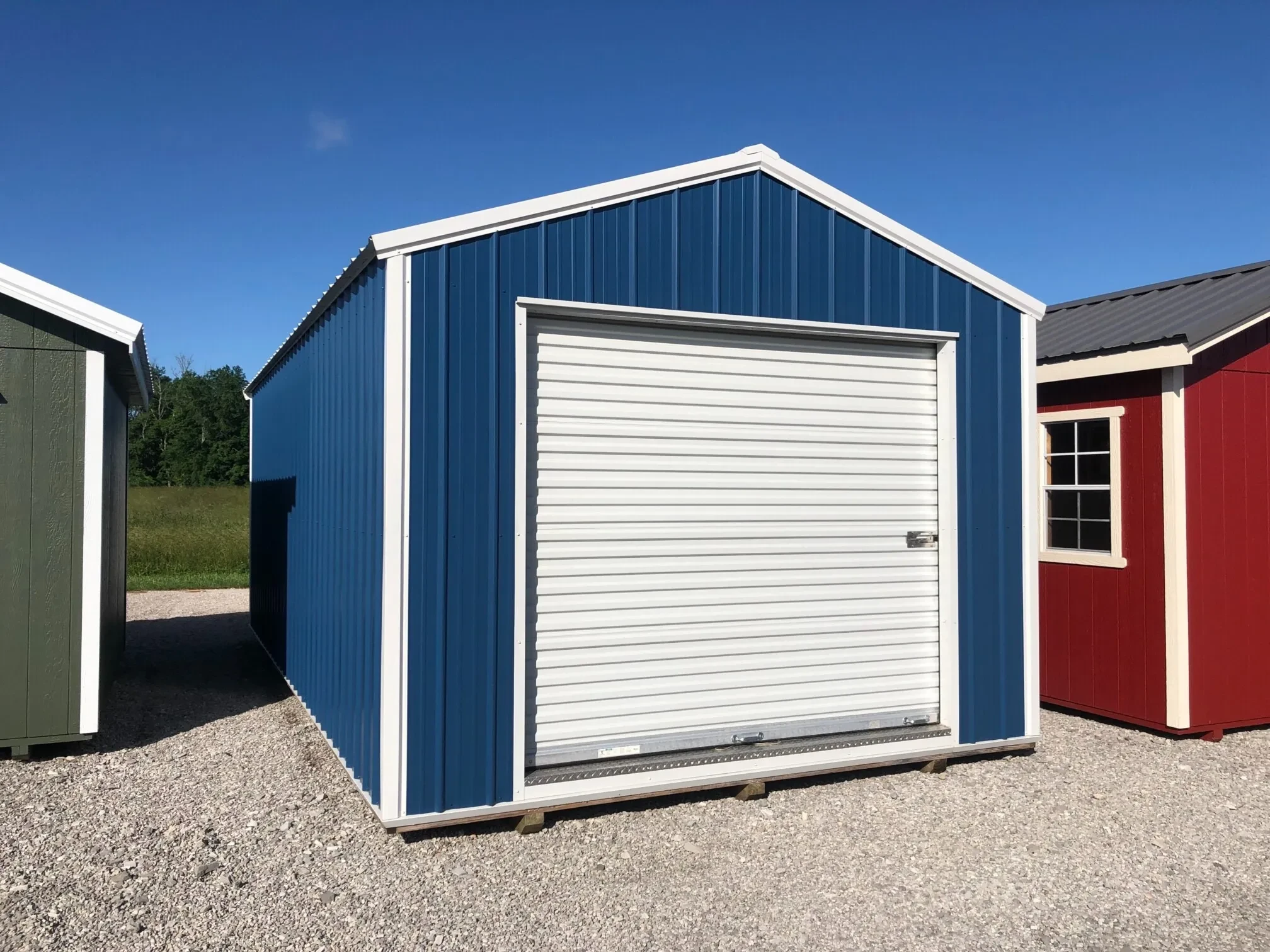 The front of a blue metal garage shed showing the rollup door in the front, as it sits between two other sheds