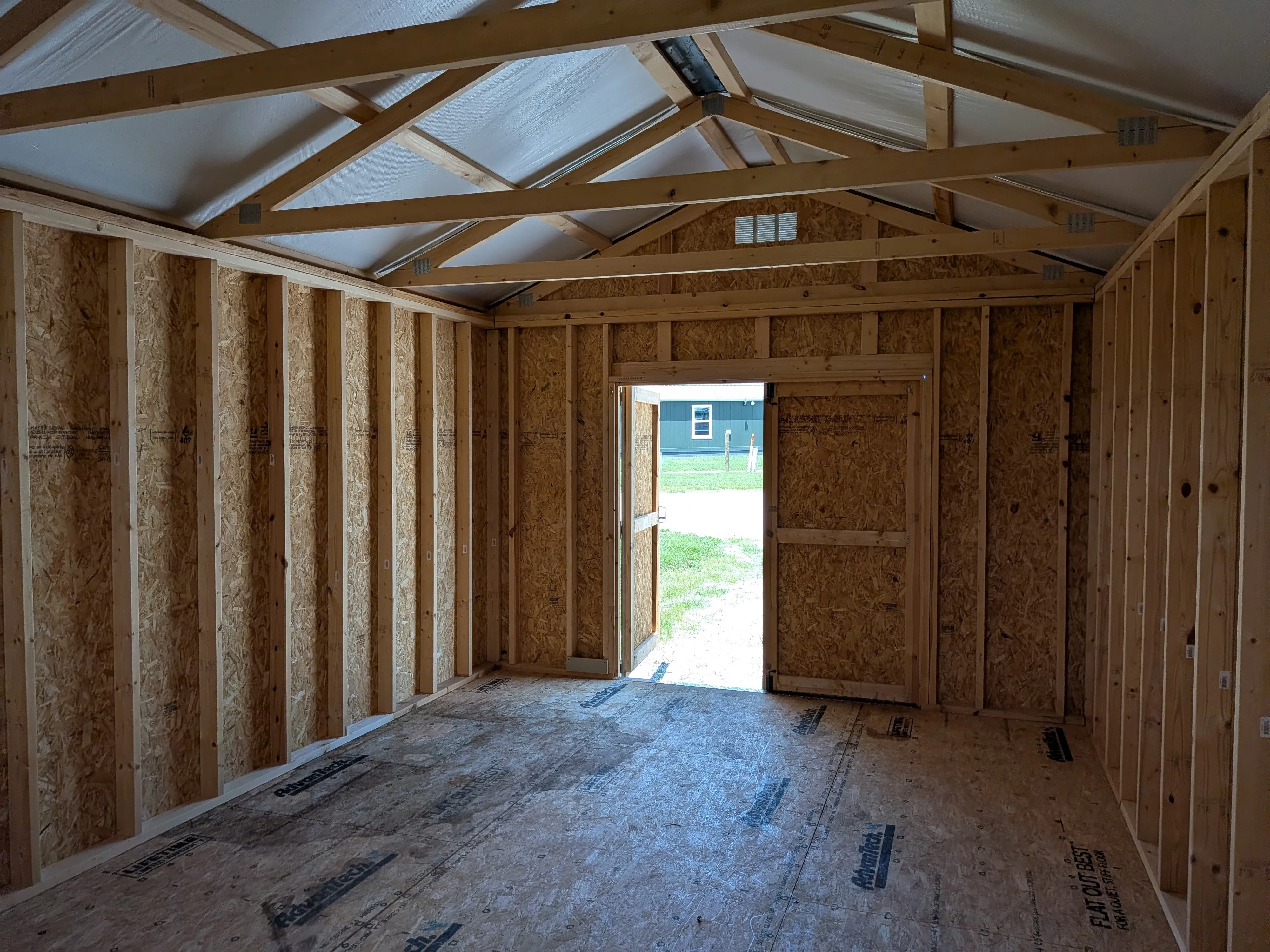 inside a wood utility shed looking at the front wall. It has double doors, one of which is open.