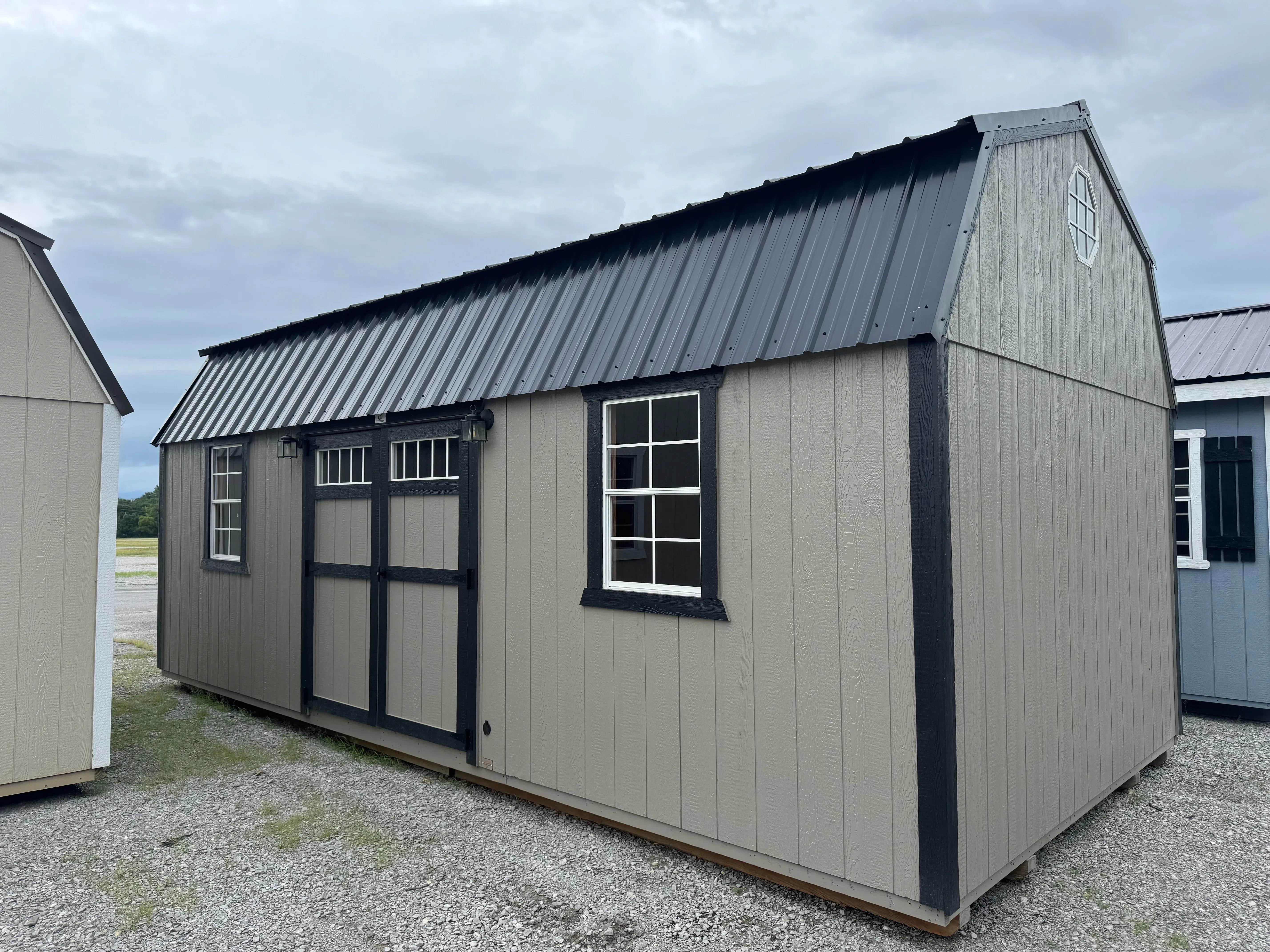 a large side lofted barn with doors and windows on the side. It is clay colored with black trim