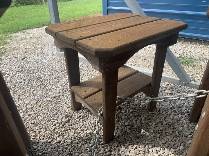 a small wood stained and sealed end table chained up and on gravel.