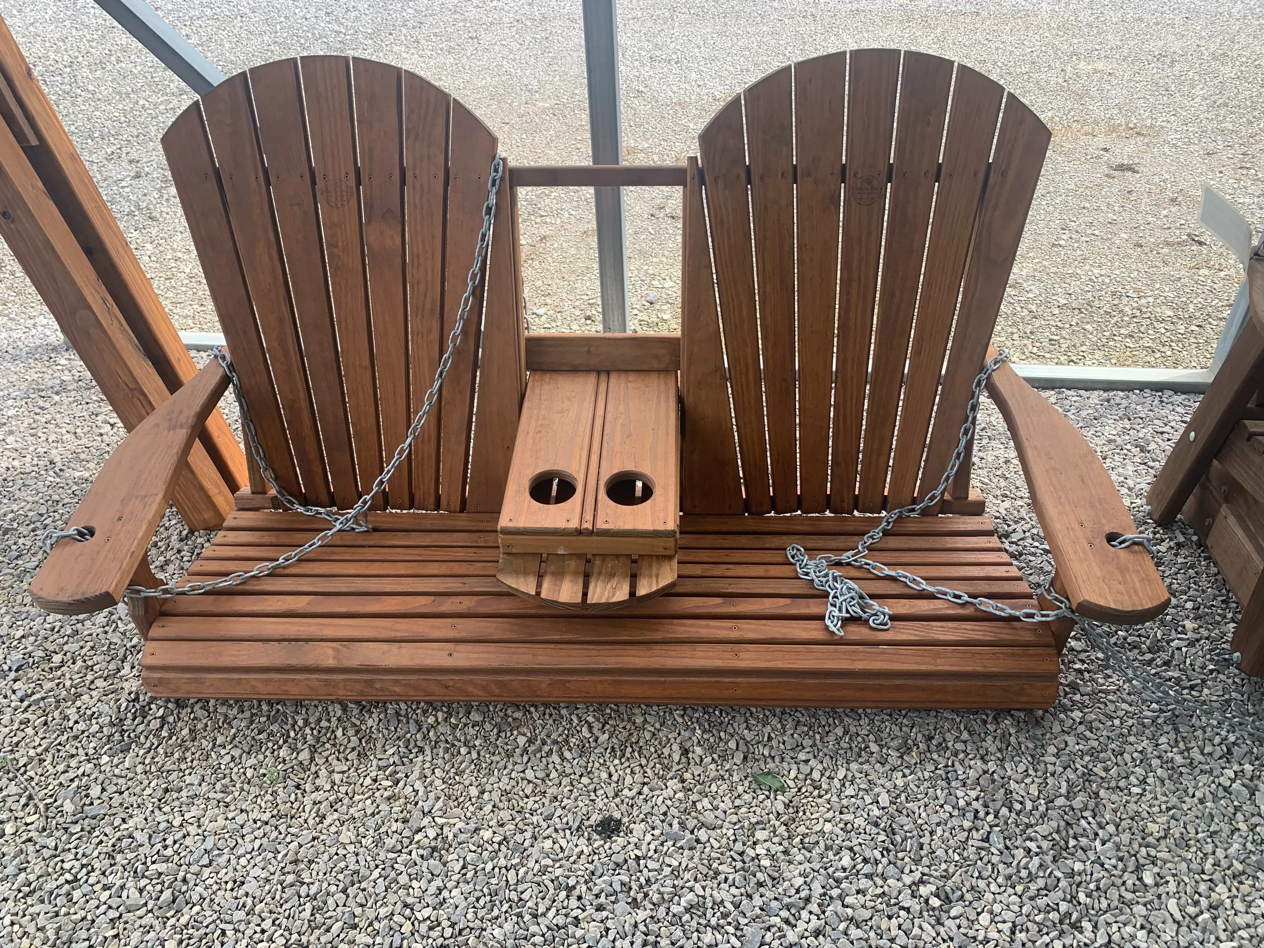 a wood stained and sealed swing with two seats and a center console that flips up and down